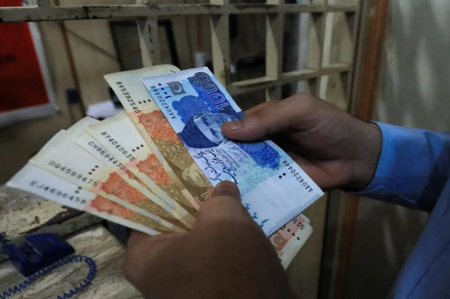 رجل يعد أوراقاً نقدية من الروبية الباكستانية بمحل صرافة في بيشاور (رويترز)