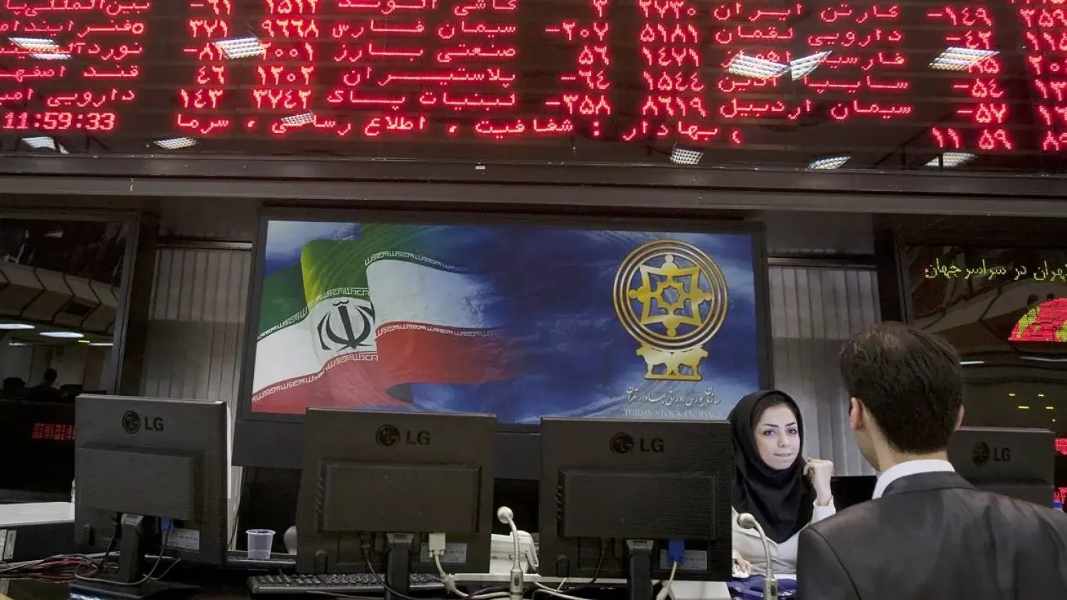 يتحدث تاجر مع موظف بسوق الأوراق المالية تحت اللوحة الإلكترونية في بورصة طهران (رويترز)