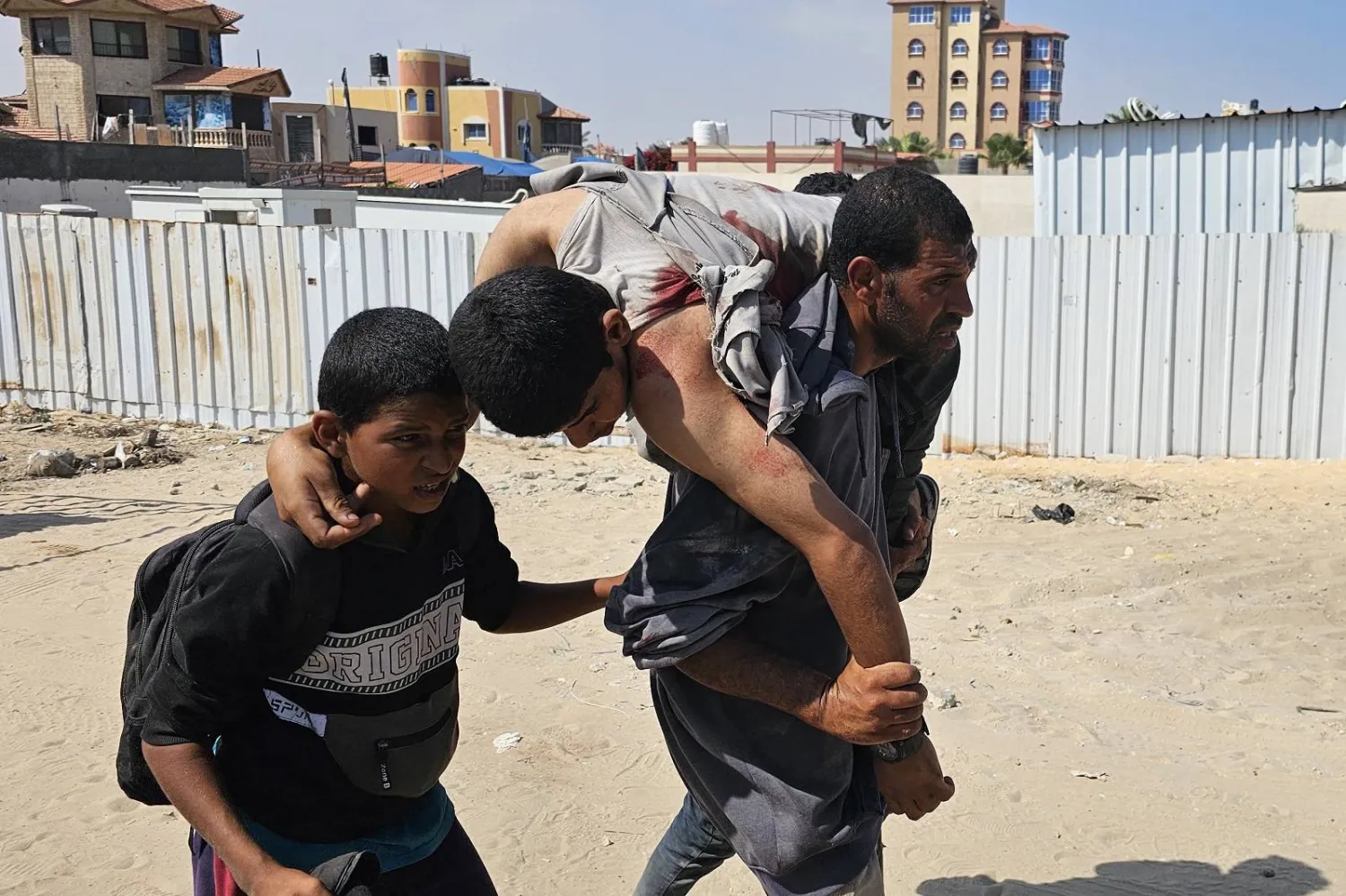 فلسطيني يحمل رجلاً مصاباً في أثناء وقوفه في طابور للحصول على المساعدة باتجاه مستشفى في رفح جنوب غزة (أ.ف.ب)