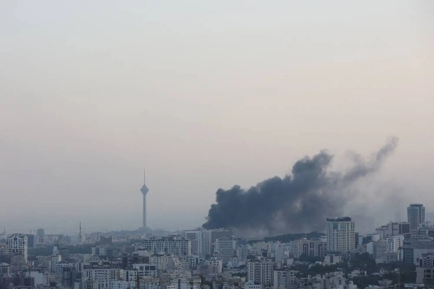 يتصاعد الدخان عقب هجوم إسرائيلي على مبنى هيئة الإذاعة والتلفزيون الإيراني، فيما يبدو في الخلفية برج ميلاد أبرز معالم العاصمة الإيرانية طهران (رويترز)