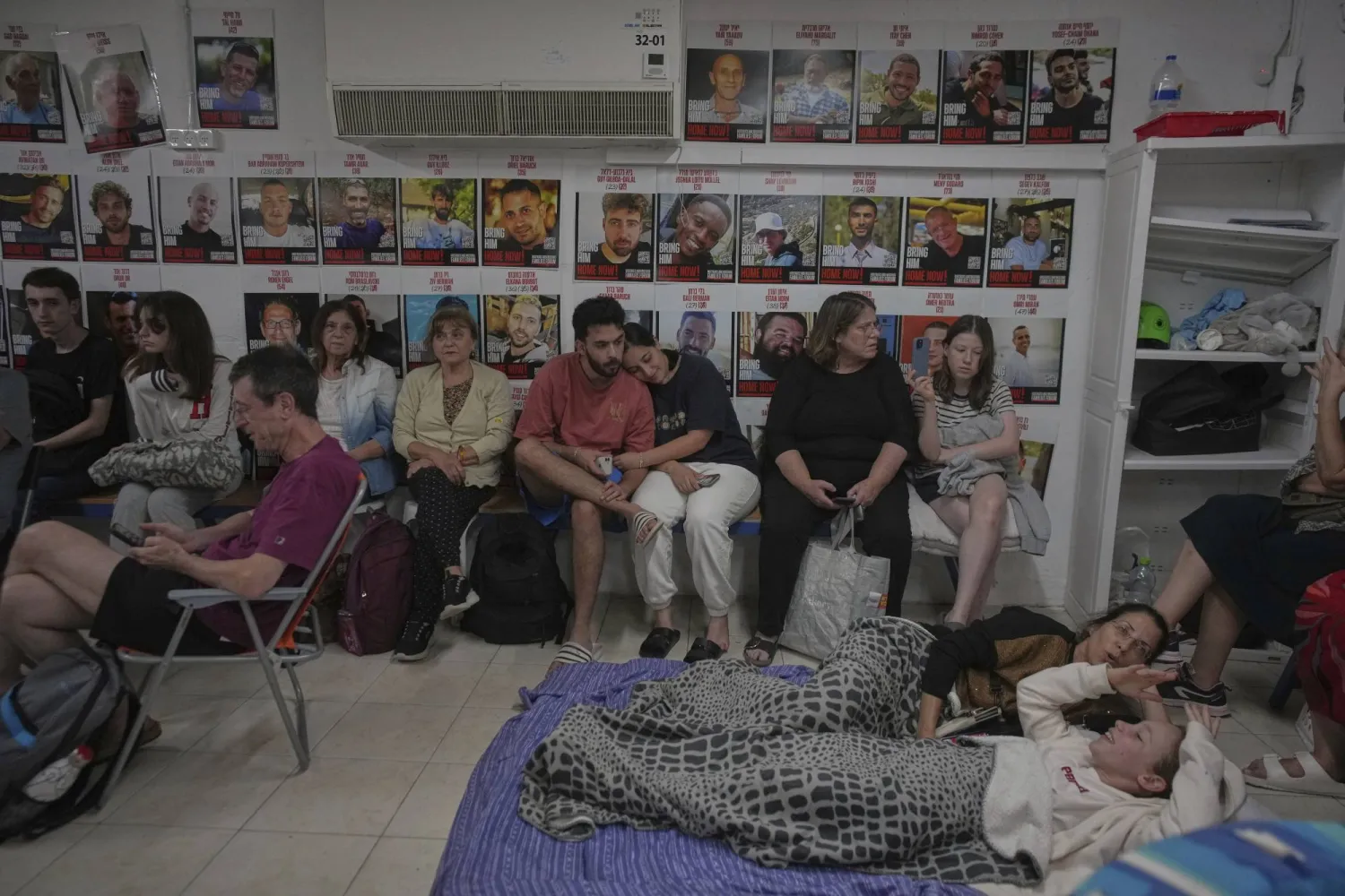 إسرائيليون يحتمون بأحد الملاجئ في تل أبيب يوم الخميس وعلى الجدار صور محتجزين إسرائيليين في غزة (أ.ب)