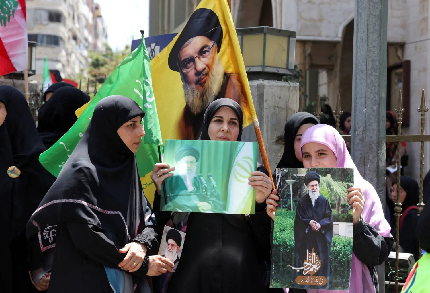 نساء يحملن صور خامنئي ونصر الله خلال مسيرة دعم لإيران في ضاحية بيروت الجنوبية الجمعة (رويترز)