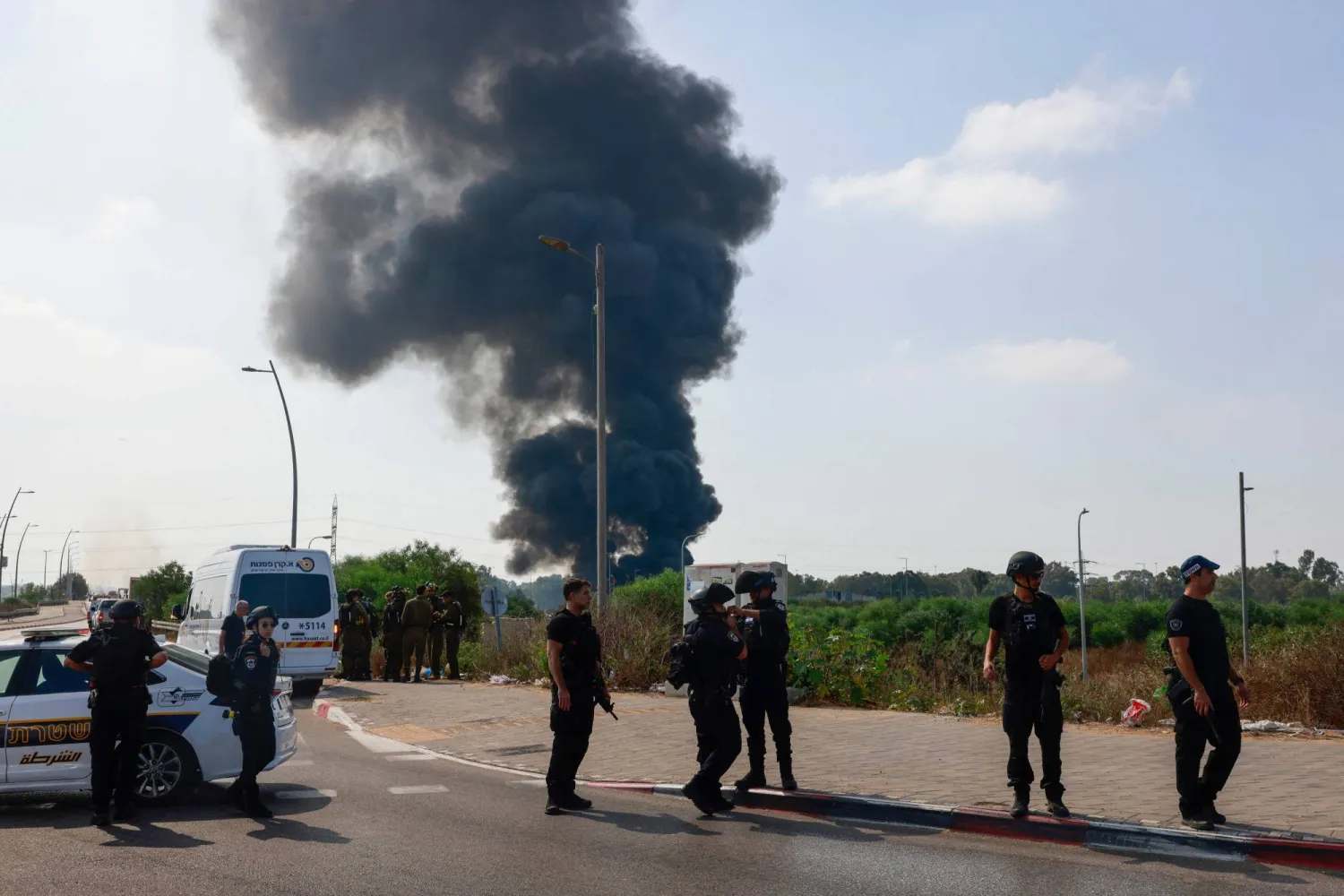 عناصر من الشرطة الإسرائيلية تقف بينما يتصاعد دخان جراء غارات إيرانية على موقع في هرتسليا قرب تل أبيب (أ.ف.ب)