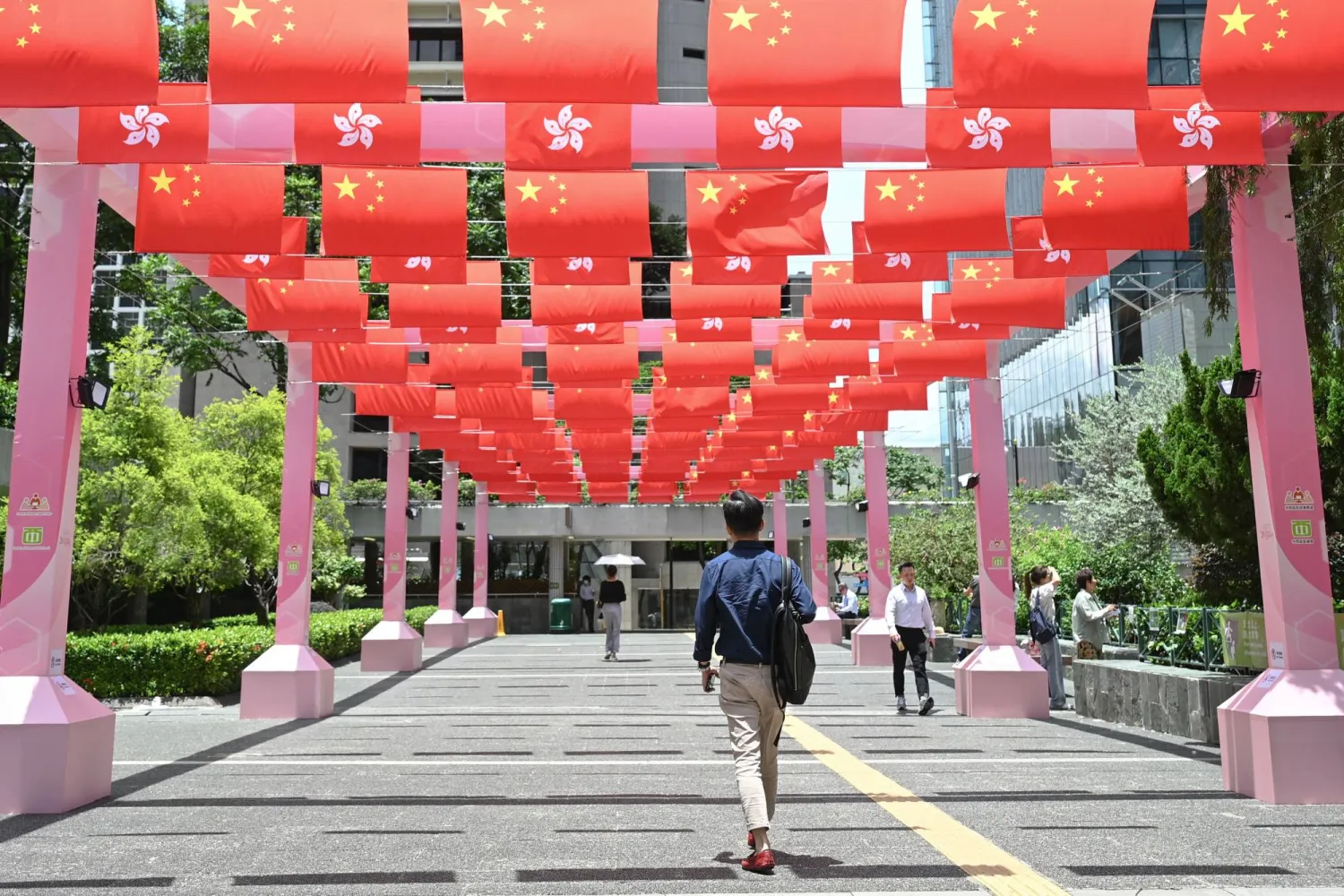 مشاة يسيرون في أحد شوارع مدينة هونغ كونغ تحت أعلام الجزيرة وأعلام الصين بمناسبة الاحتفال بذكرى عودة الجزيرة إلى السيادة الصينية (أ.ف.ب)