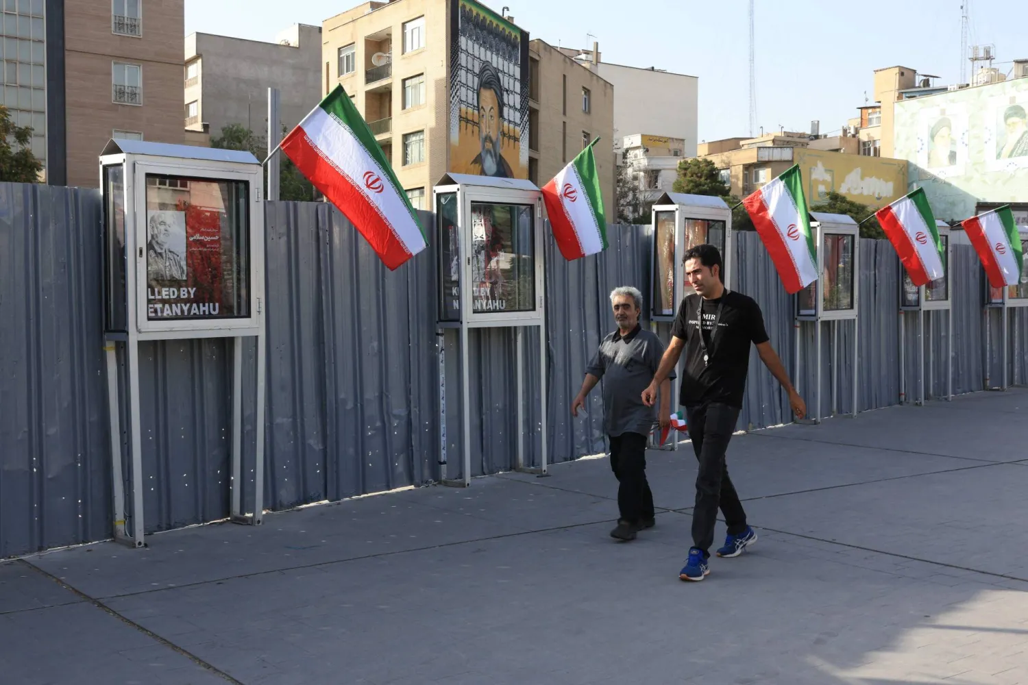 رجلان إيرانيان يمران أمام صور في نصب تذكاري لأولئك الذين قُتلوا على يد إسرائيل في طهران (أ.ف.ب)