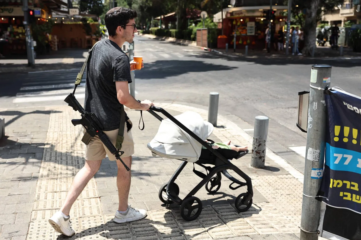 إسرائيلي مسلح يدفع عربة أطفال يوم الثلاثاء في تل أبيب (أ.ف.ب) 