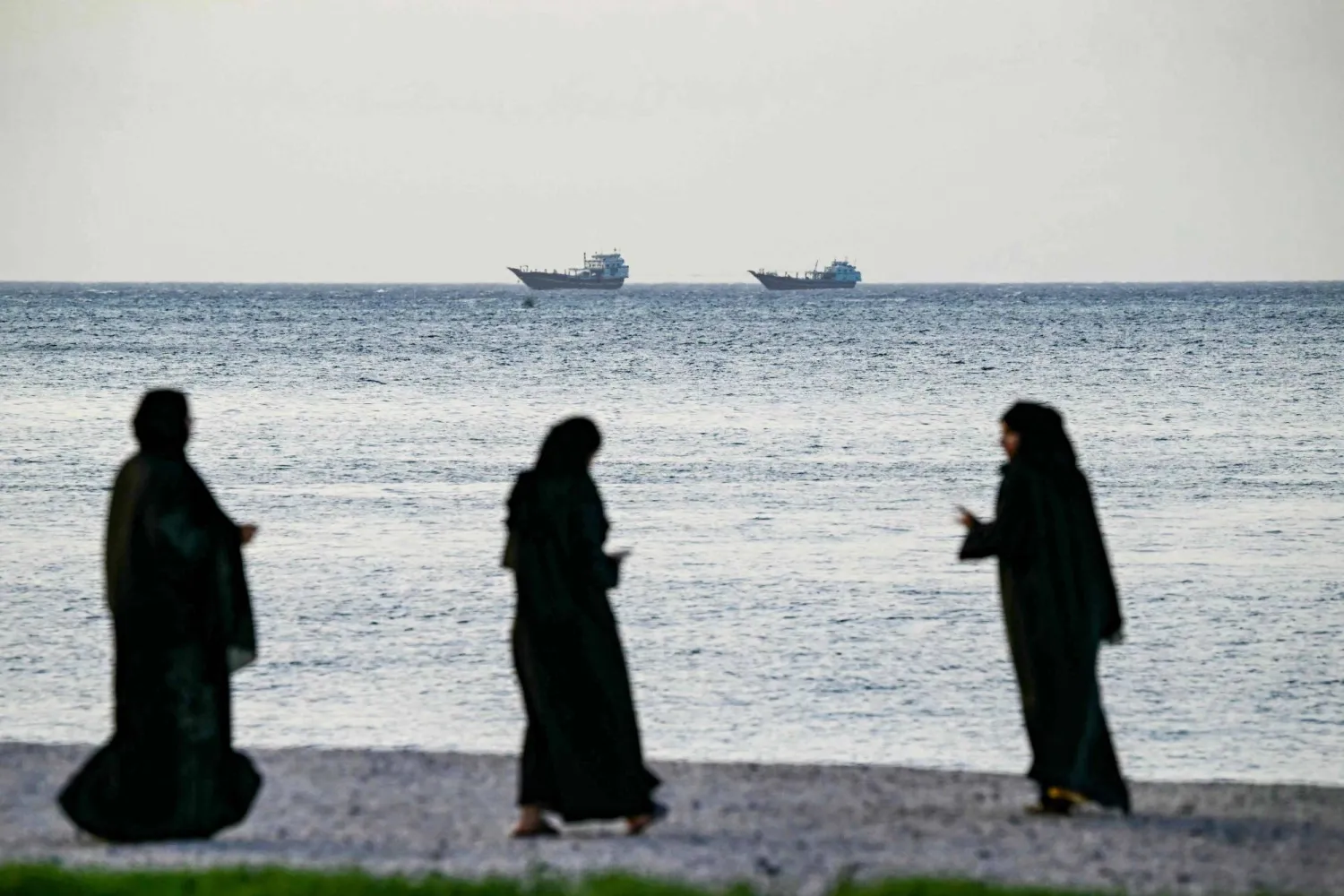 نساءٌ يسِرن على شاطئ خصب شمال شبه جزيرة مسندم في عُمان المطلة على مضيق هرمز (أ.ف.ب)