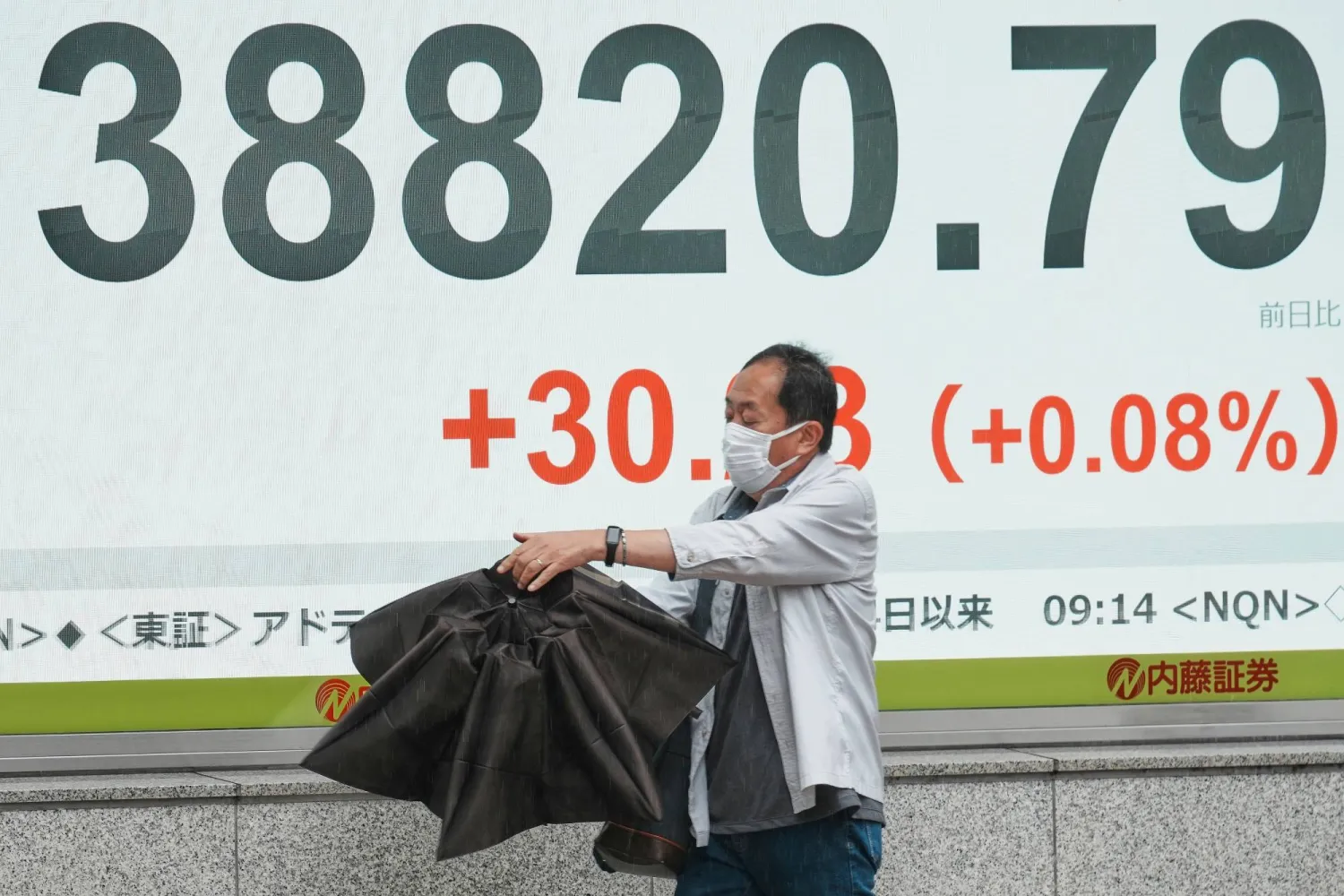 رجل يضبط مظلته في حين يمر أمام شاشة تعرض حركة الأسهم وسط العاصمة اليابانية طوكيو (أ.ب)