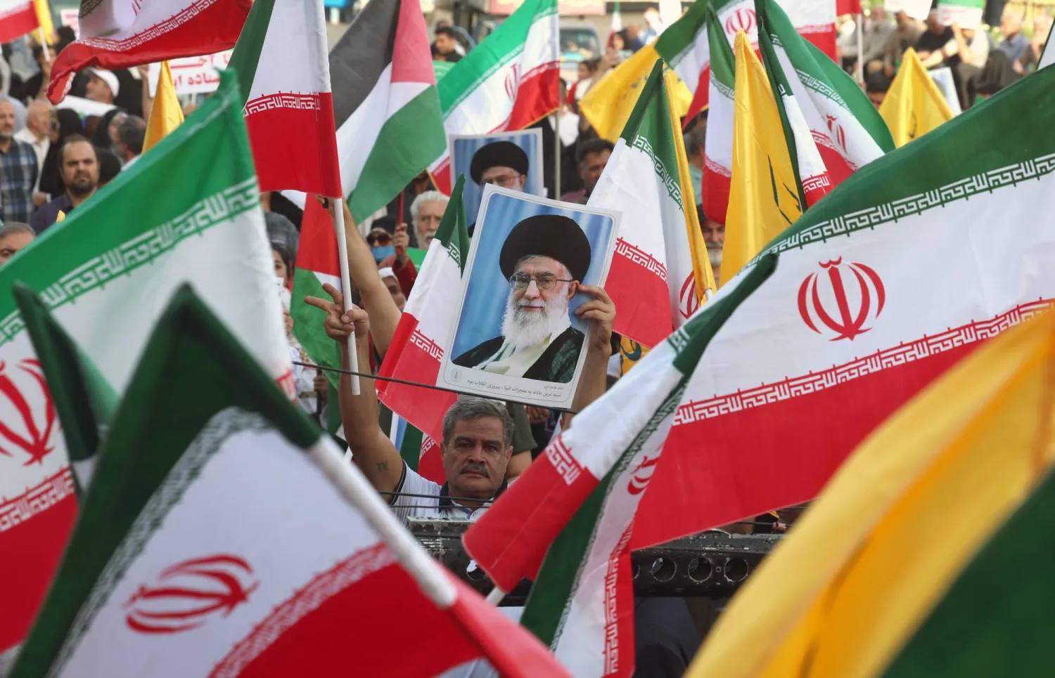 رجل يحمل صورة المرشد الإيراني علي خامنئي وسط الأعلام الوطنية الإيرانية خلال تجمع في طهران (إ.ب.أ)