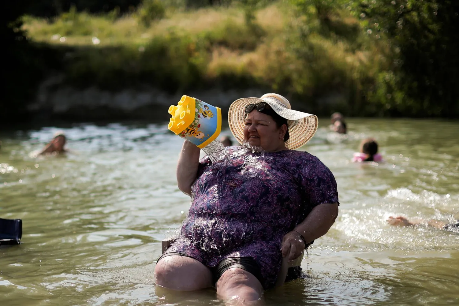 سيدة تجلس وسط مياه نهر إيرينيك في كوسوفو وتصب المياه على جسدها لتبريده وسط موجة حر (رويترز)