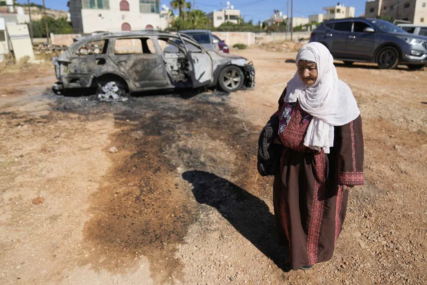 فلسطينية تمر أمام سيارة محترقة من جراء هجوم إسرائيلي استهدف قرية كفر مالك شرق رام الله الخميس (أ.ب)