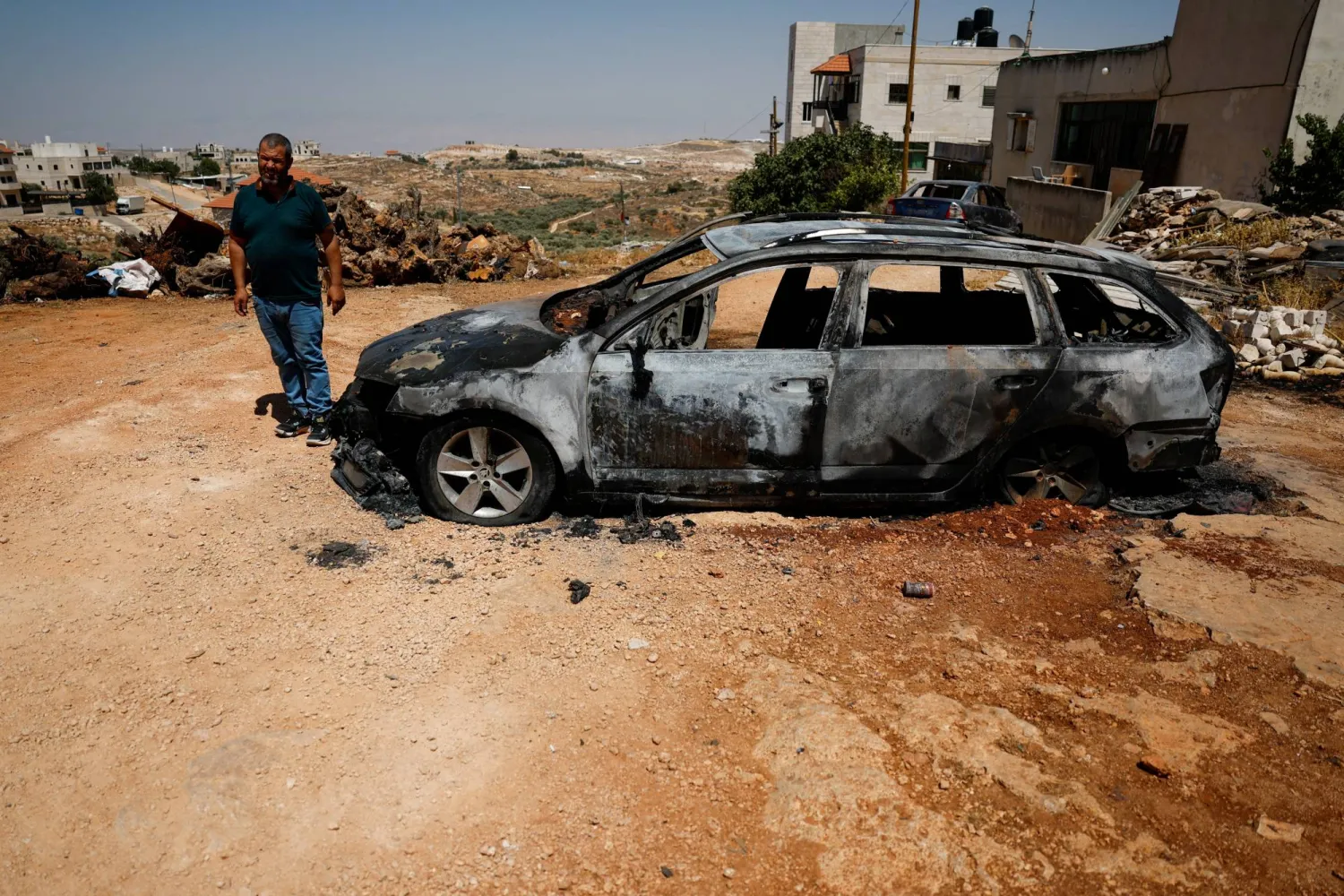 فلسطيني يقف بجوار سيارة محترقة بعد هجوم شنّه مستوطنون إسرائيليون في كفر مالك بالضفة الغربية (رويترز)