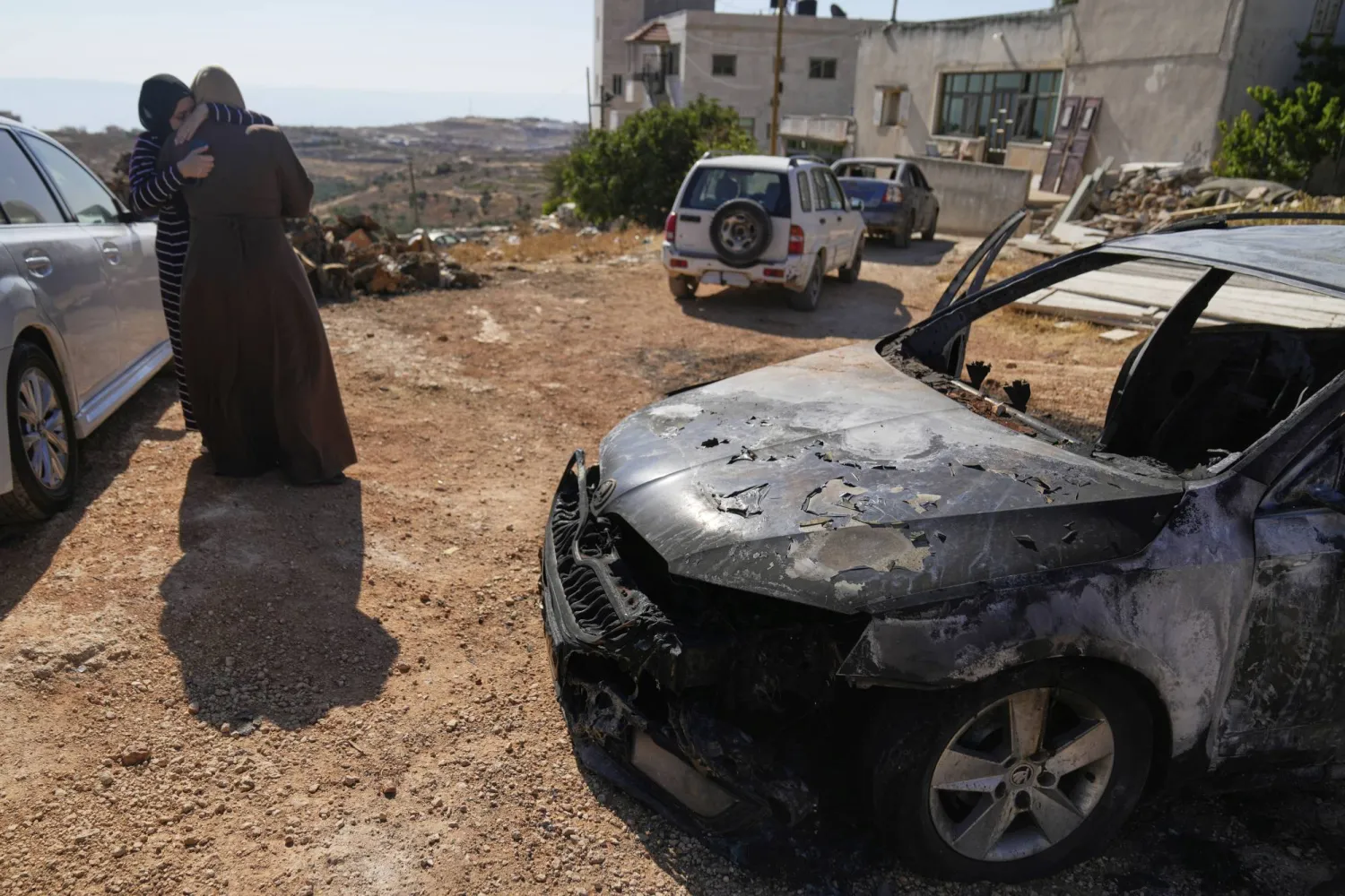 نساء يواسين بعضهن بعد هجوم أسفر عن مقتل 3 فلسطينيين وحرق كثير من السيارات وإتلاف المنازل في قرية كفر مالك بالضفة الغربية الأربعاء (أ.ب)