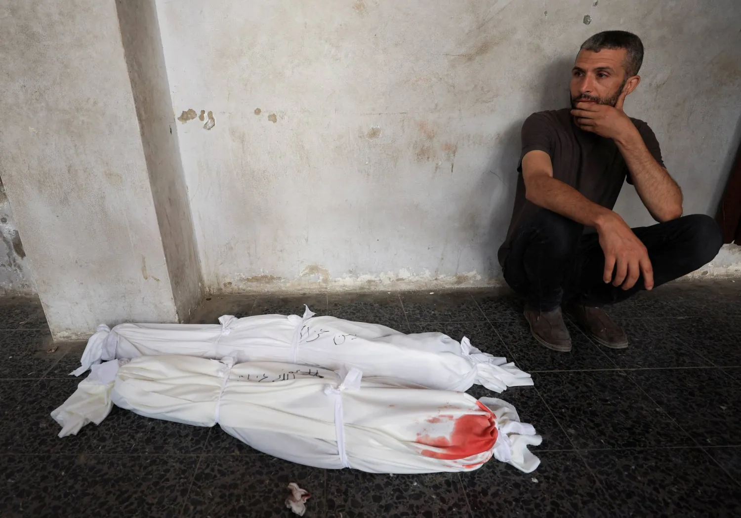 فلسطيني يجلس قرب جثث أطفال قُتلوا بغارة إسرائيلية على منزل قبل تشييعهم من مستشفى في مدينة غزة يوم الأحد (رويترز)