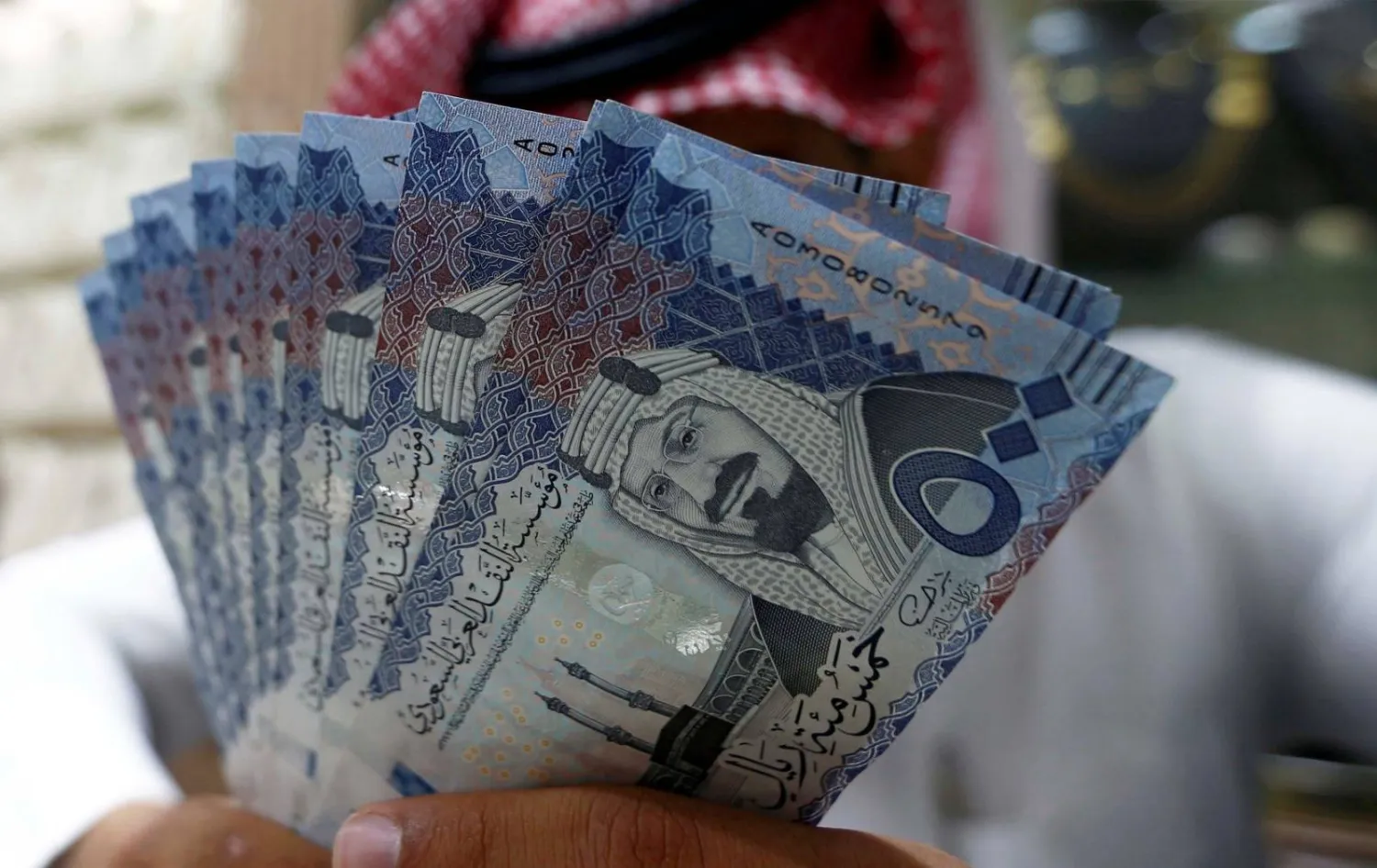 صراف سعودي يعرض أوراقاً نقدية بالريال السعودي في محل صرافة (رويترز)