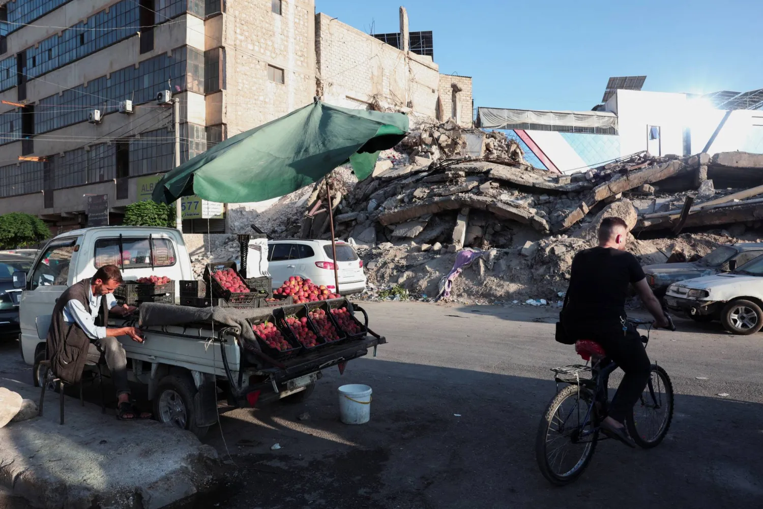 رجل على دراجة هوائية يعبر عربة خضراوات ومبنى مدمراً في حلب من فترة الحرب التي كانت القوات الروسية طرفاً فيها (رويترز)