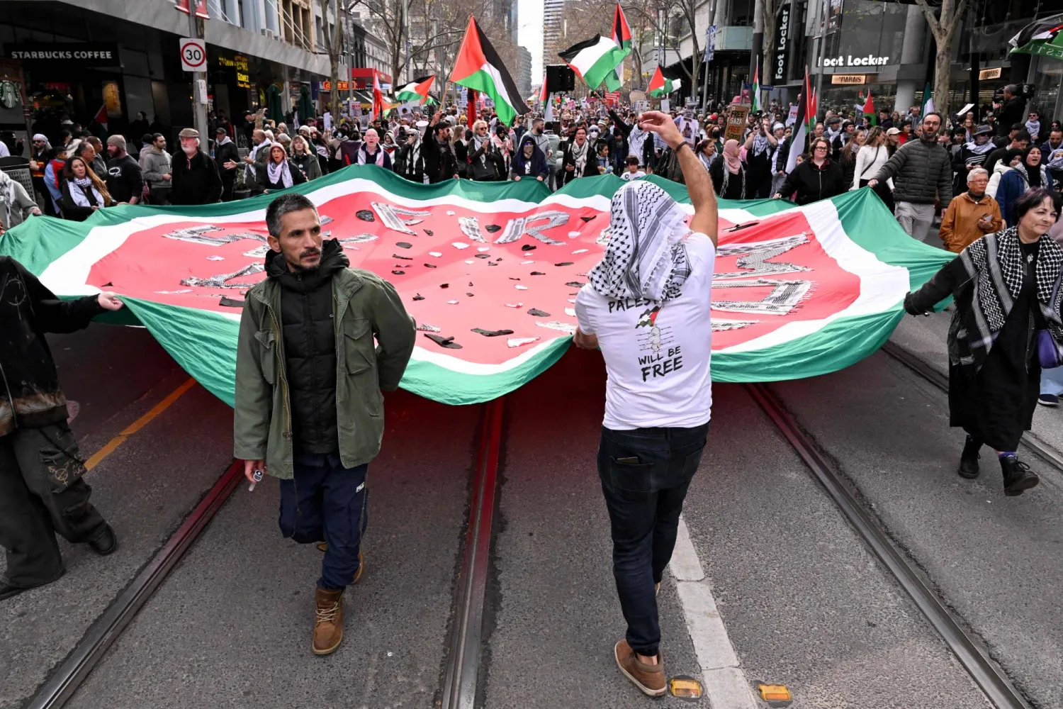 يحمل الناس لافتات ويلوحون بالأعلام خلال مسيرة مؤيدة للفلسطينيين في شوارع ملبورن يوم 6 يوليو 2025 (أ.ف.ب)