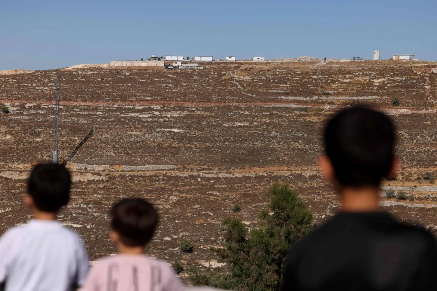 أطفال فلسطينيون قبالة بؤرة استيطانية إسرائيلية جديدة اقيمت شمال الخليل في الضفة الغربية المحتلة، في 6 يوليو/تموز 2025 (أ ف ب)