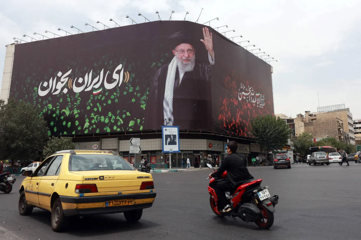 سيارات تمر بجانب لوحة تحمل صورة خامنئي وعبارة «يا إيران» في ساحة انقلاب (الثورة) وسط طهران (أ.ف.ب)
