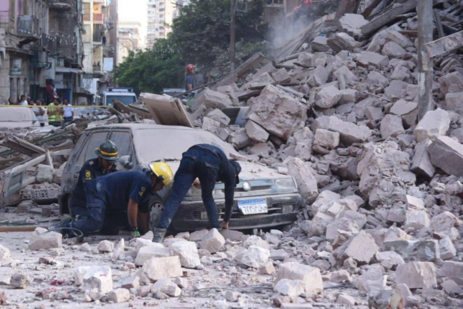 أفراد من الخدمة المدنية يحاولون رفع سيارة من وسط الهدم في موقع العقار بالإسكندرية (الصفحة الرسمية للمحافظة بـ«فيسبوك»)