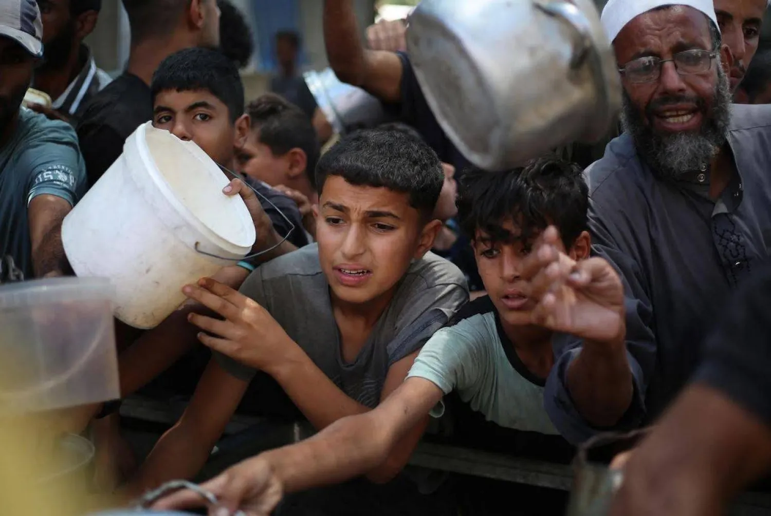 أطفال فلسطينيون يصطفون للحصول على حصة من الطعام الساخن الذي يوزعه مطبخ خيري في مخيم النصيرات للاجئين وسط غزة (أ.ف.ب)