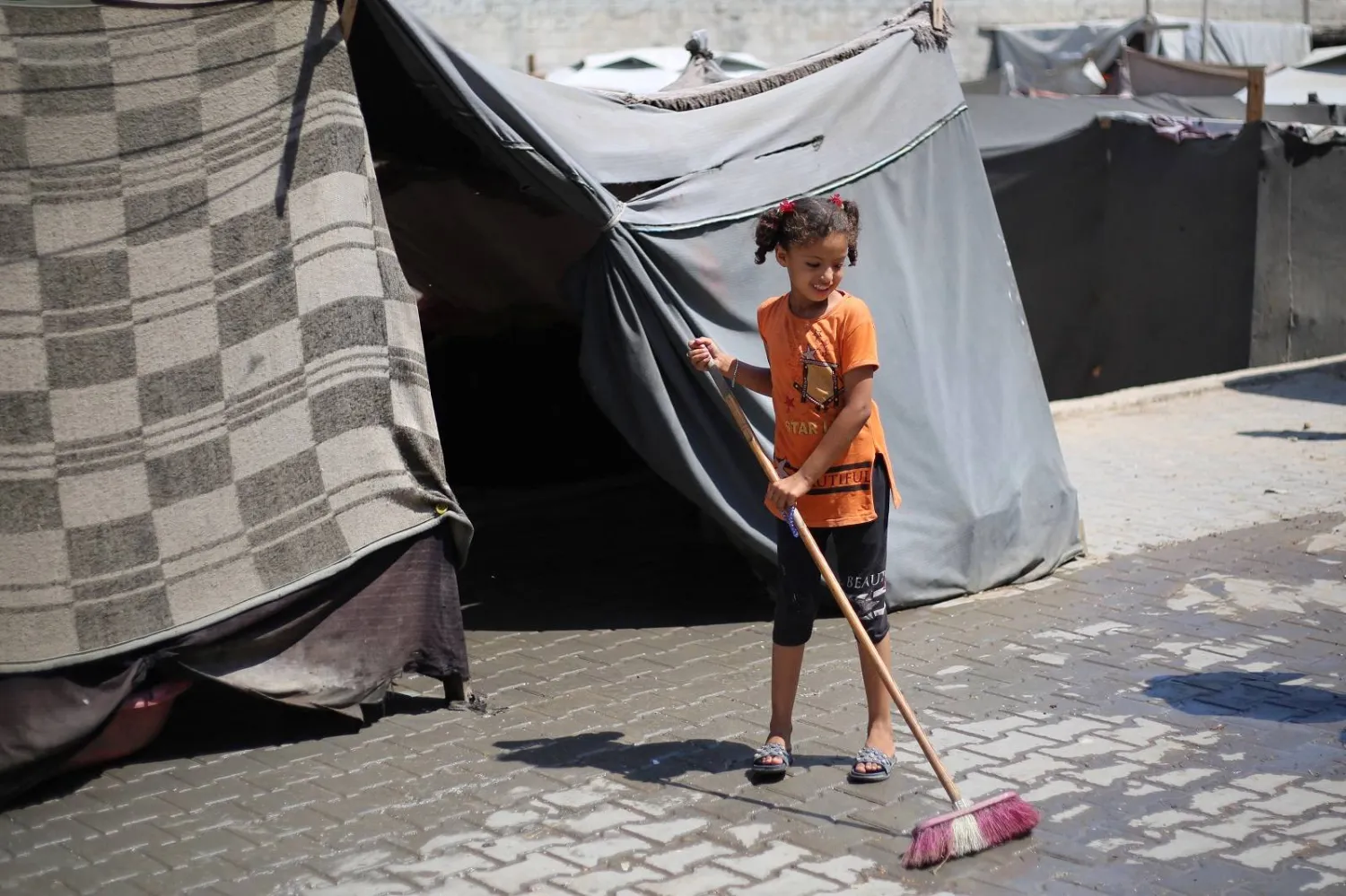 فتاة فلسطينية تكنس أمام مأواها المؤقت في مخيم النصيرات للاجئين في وسط قطاع غزة (أ.ف.ب)