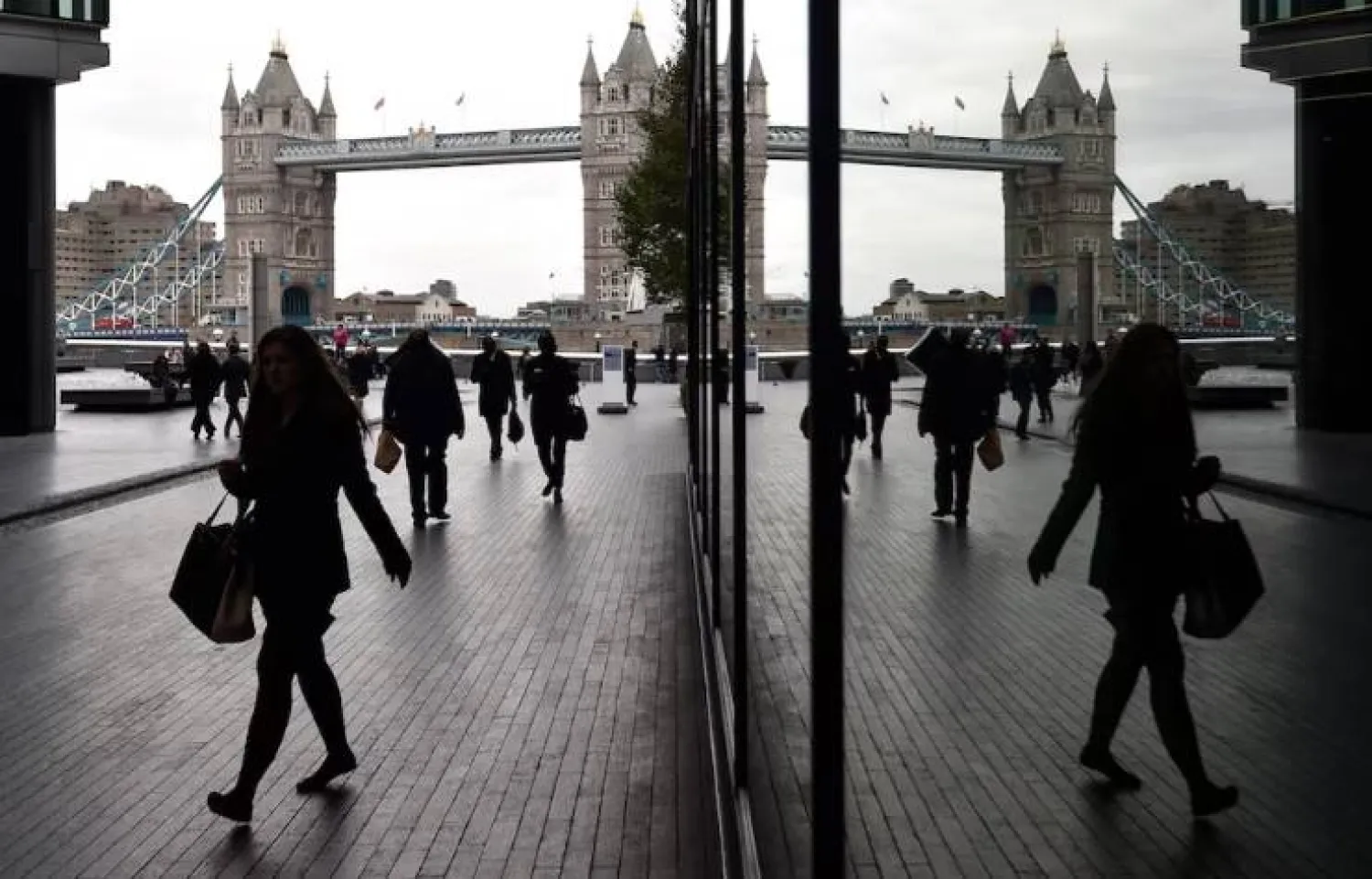 يمشي موظفون بمنطقة «مور لندن» التجارية حيث يظهر جسر «البرج» الشهير في الخلفية (أرشيفية - رويترز)
