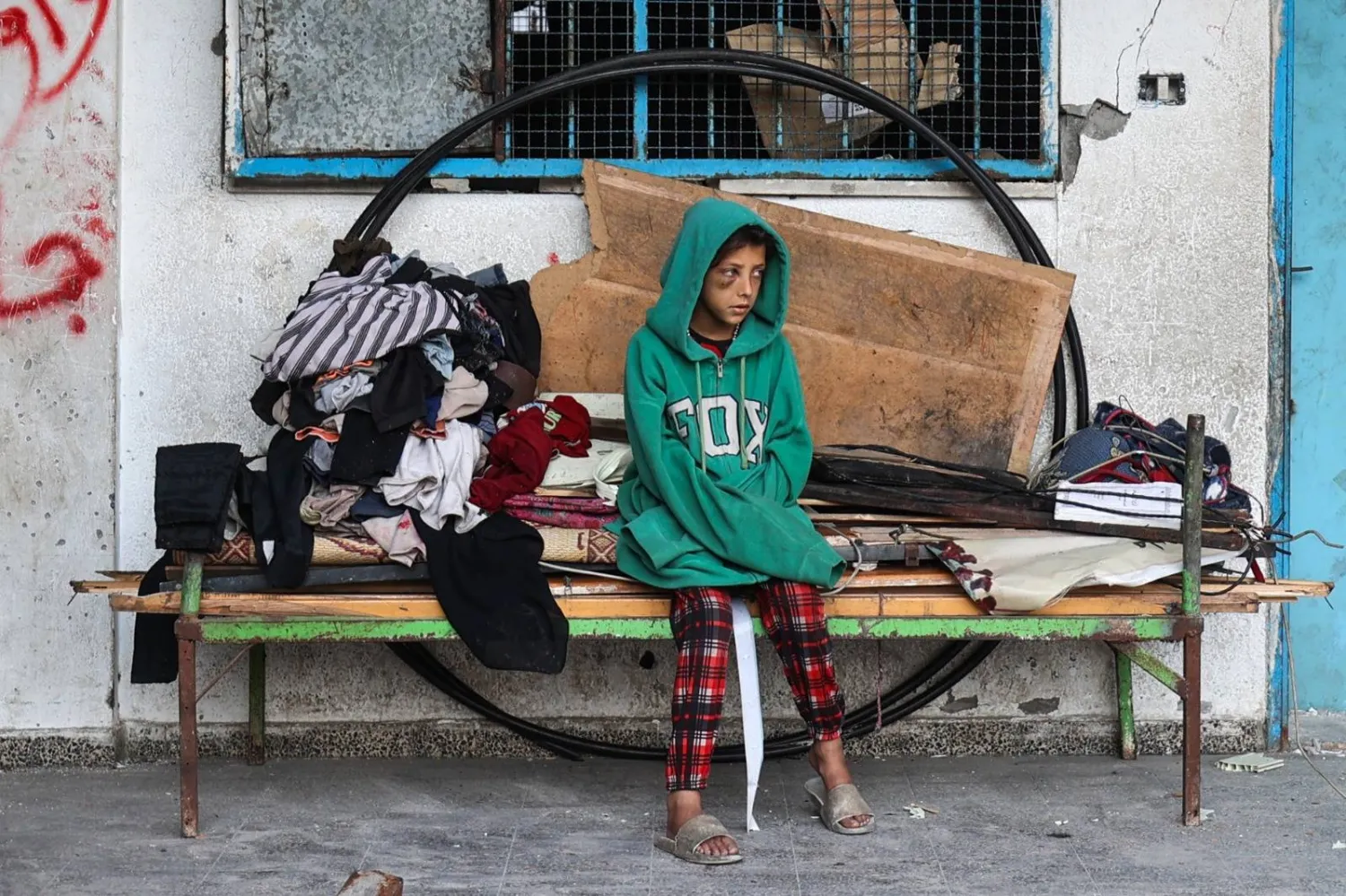 فتاة فلسطينية تنظر إلى الآخرين وهم يزيلون الحطام من مخيم مؤقت للنازحين تعرض لقصف إسرائيلي في مخيم البريج للاجئين (أ.ف.ب)