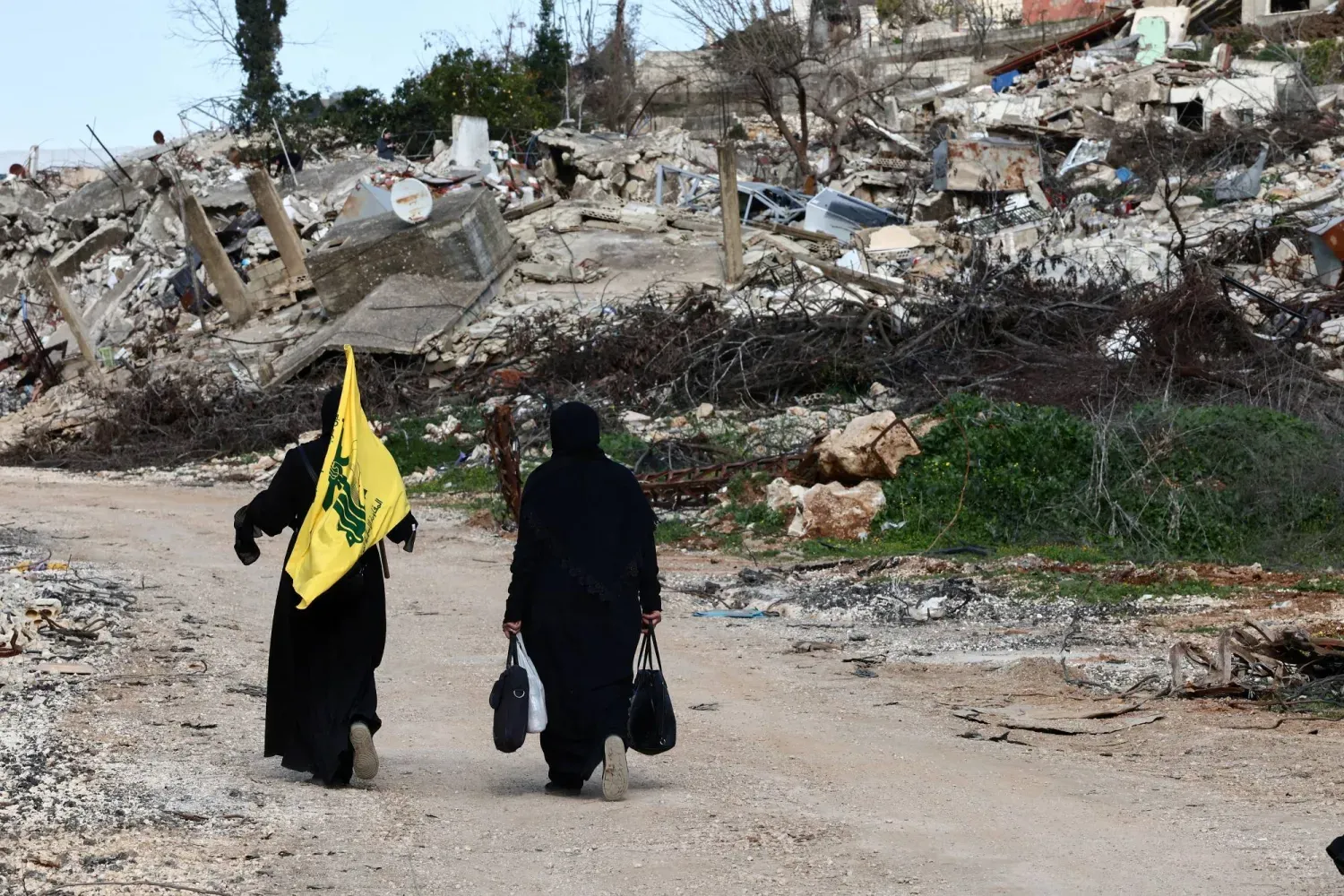 İki Hizbullah destekçisi Kafr Kila'da İsrail bombardımanından kalan enkazın yanından geçerken (Arşiv- Reuters)
