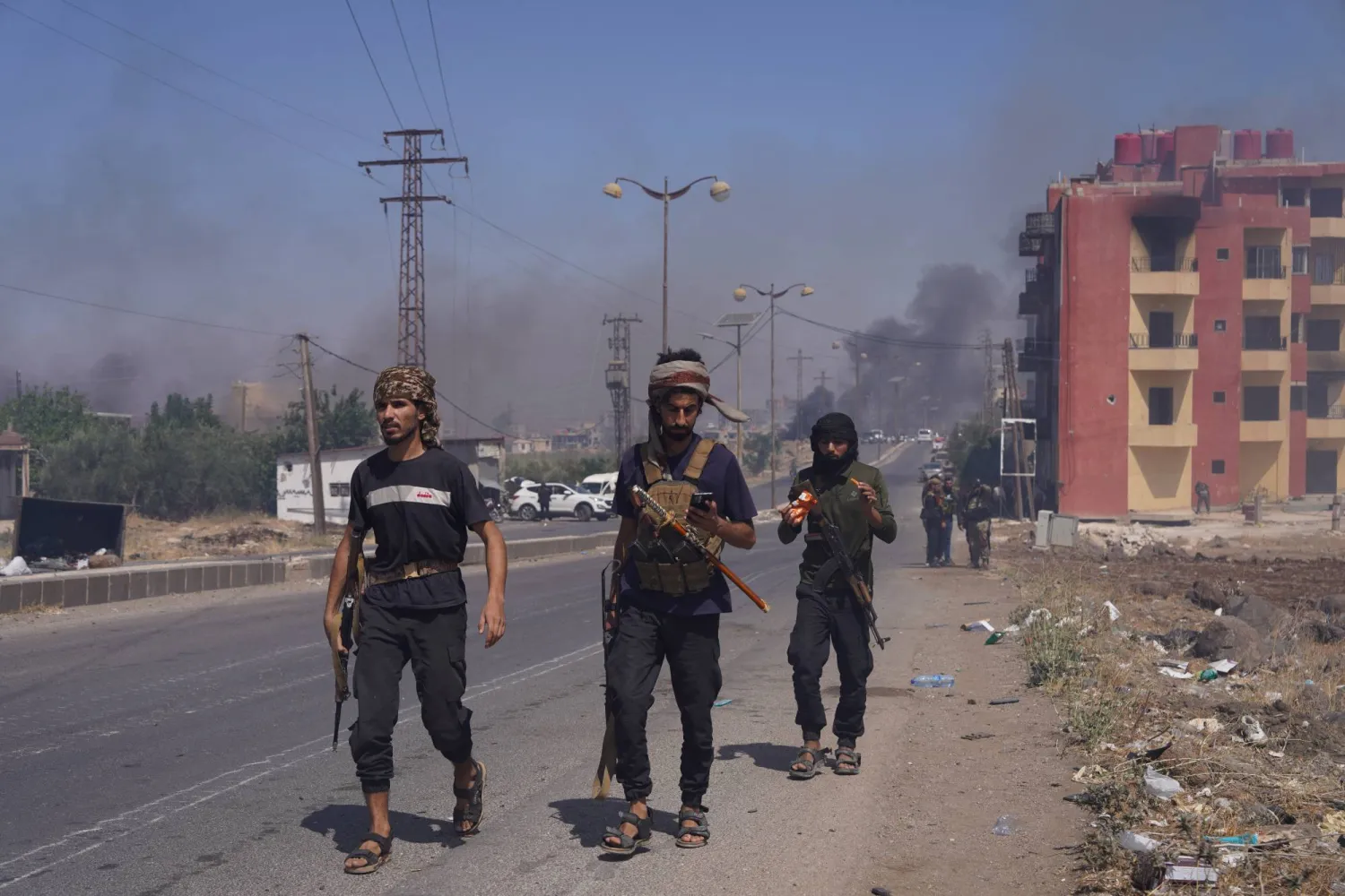 يتصاعد الدخان فيما يسير مقاتلون بدو على طول الشارع حاملين أسلحتهم عقب إعلان الرئاسة السورية وقف إطلاق النار بعد أيام من العنف في محافظة السويداء (رويترز)