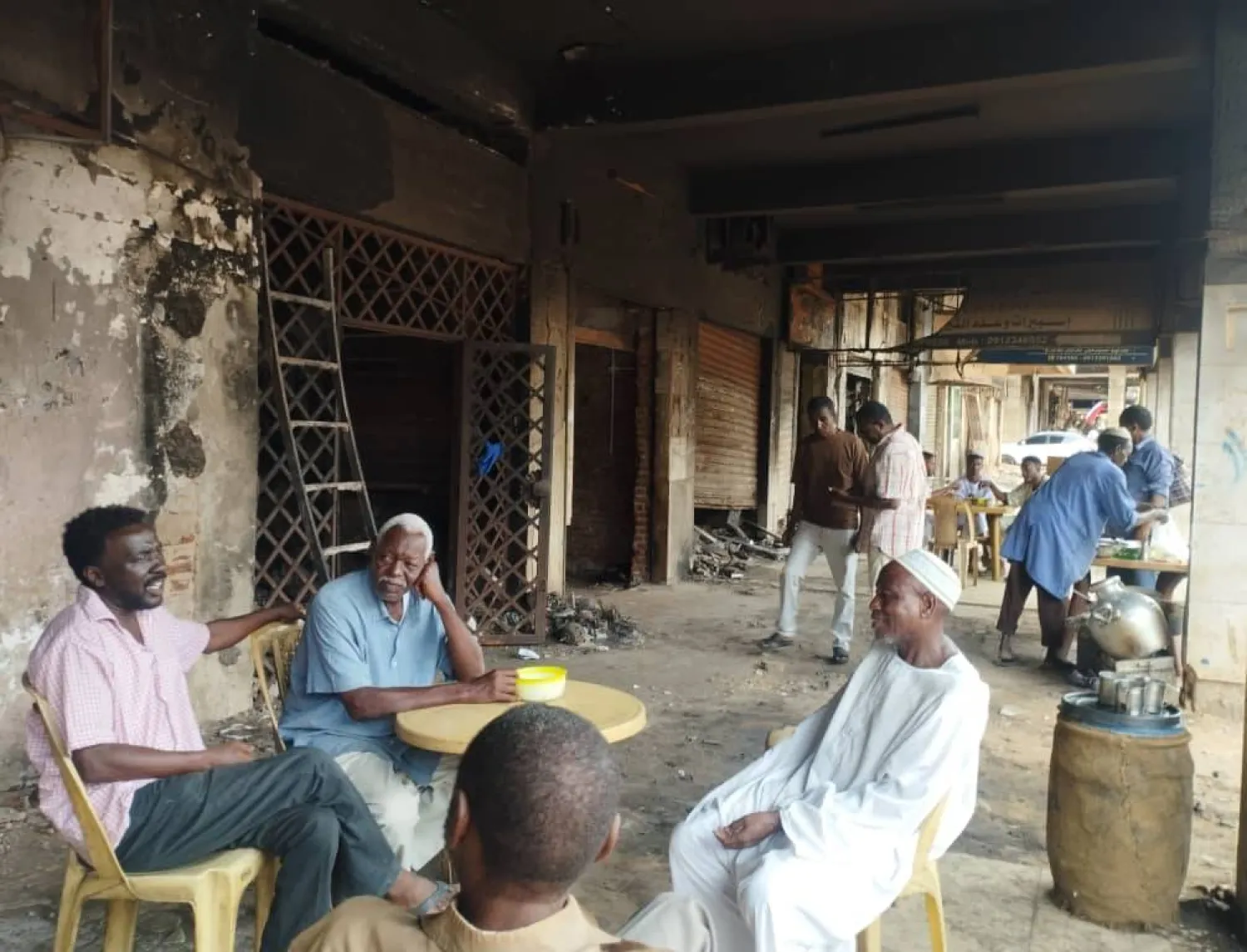 تجار يجتمعون أمام متاجرهم المحترقة في إحدى الصالات التجارية بالخرطوم (الشرق الأوسط)