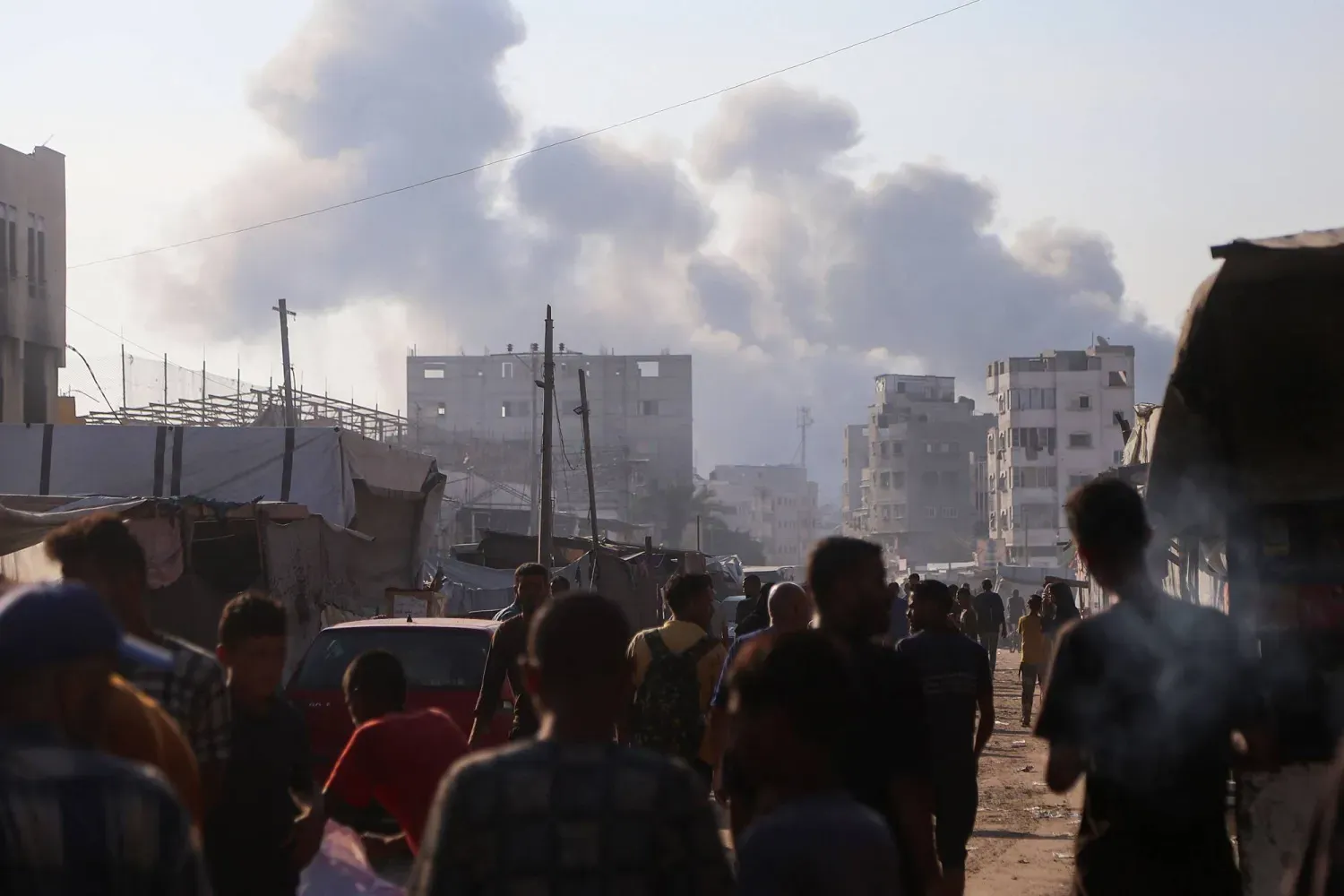 Yerinden edilmiş Filistinliler, İsrail'in Gazze Şeridi'nin güneyindeki Han Yunus'a düzenlediği hava saldırıları sırasında yükselen duman sütunlarını izliyor (AFP)