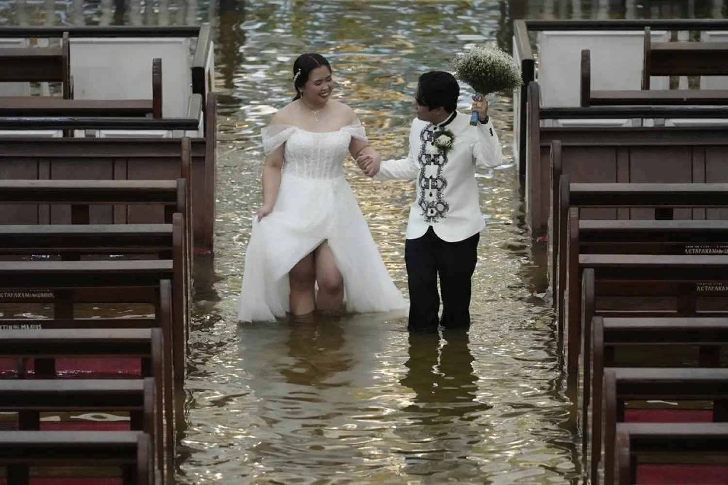 Newlyweds Jade Rick Verdillo right, and Jamaica walk hand in hand during their wedding at the flooded Barasoain church in Malolos, Bulacan province, Philippines on Tuesday, July 22, 2025. (AP Photo/Aaron Favila) 
