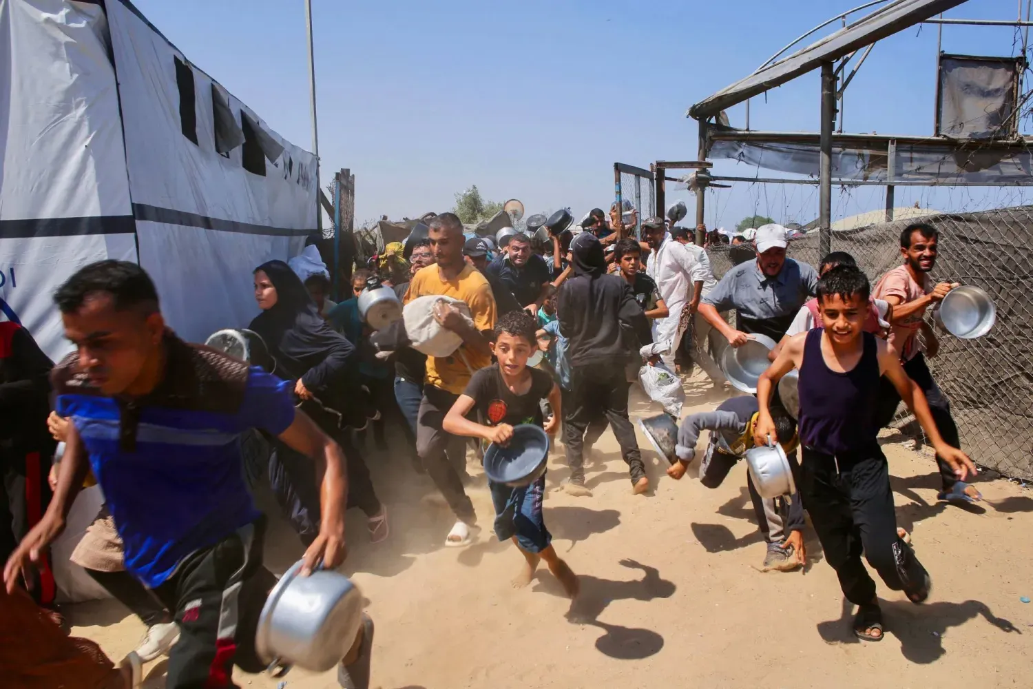 Çocuklar dün Gazze Şeridi'nin güneyindeki Han Yunus'un Mevasi bölgesinde yemek almak için acele ediyor (AFP)