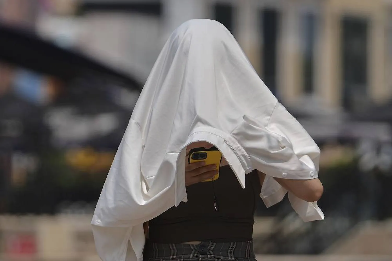 A woman covers herself from the sun as she browses a smartphone on a street during a hot day in Beijing, Wednesday, July 23, 2025. (AP)