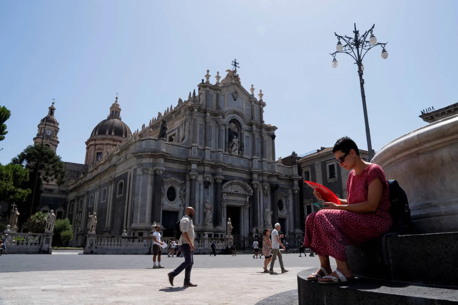 امرأة تستخدم مروحة قابلة للطي أمام كاتدرائية سانت أجاتا خلال موجة الحر في كاتانيا بإيطاليا (رويترز)