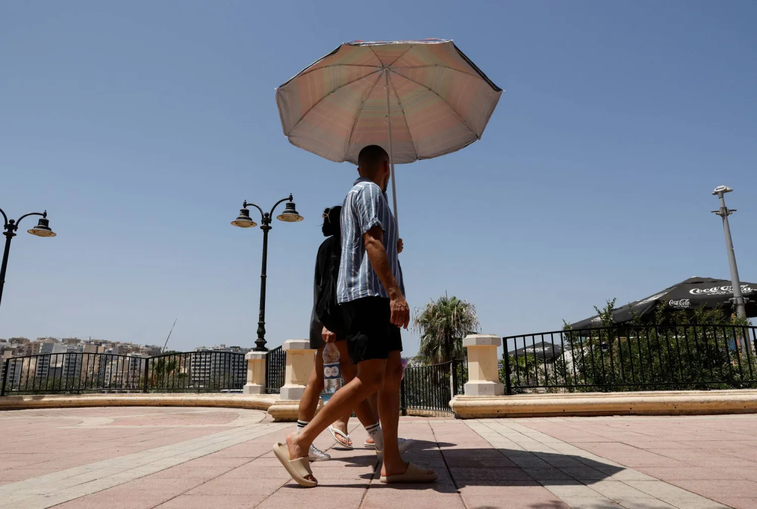رجل يستخدم مظلة للحماية من الشمس خلال المشي على طول الكورنيش في مالطا (رويترز)
