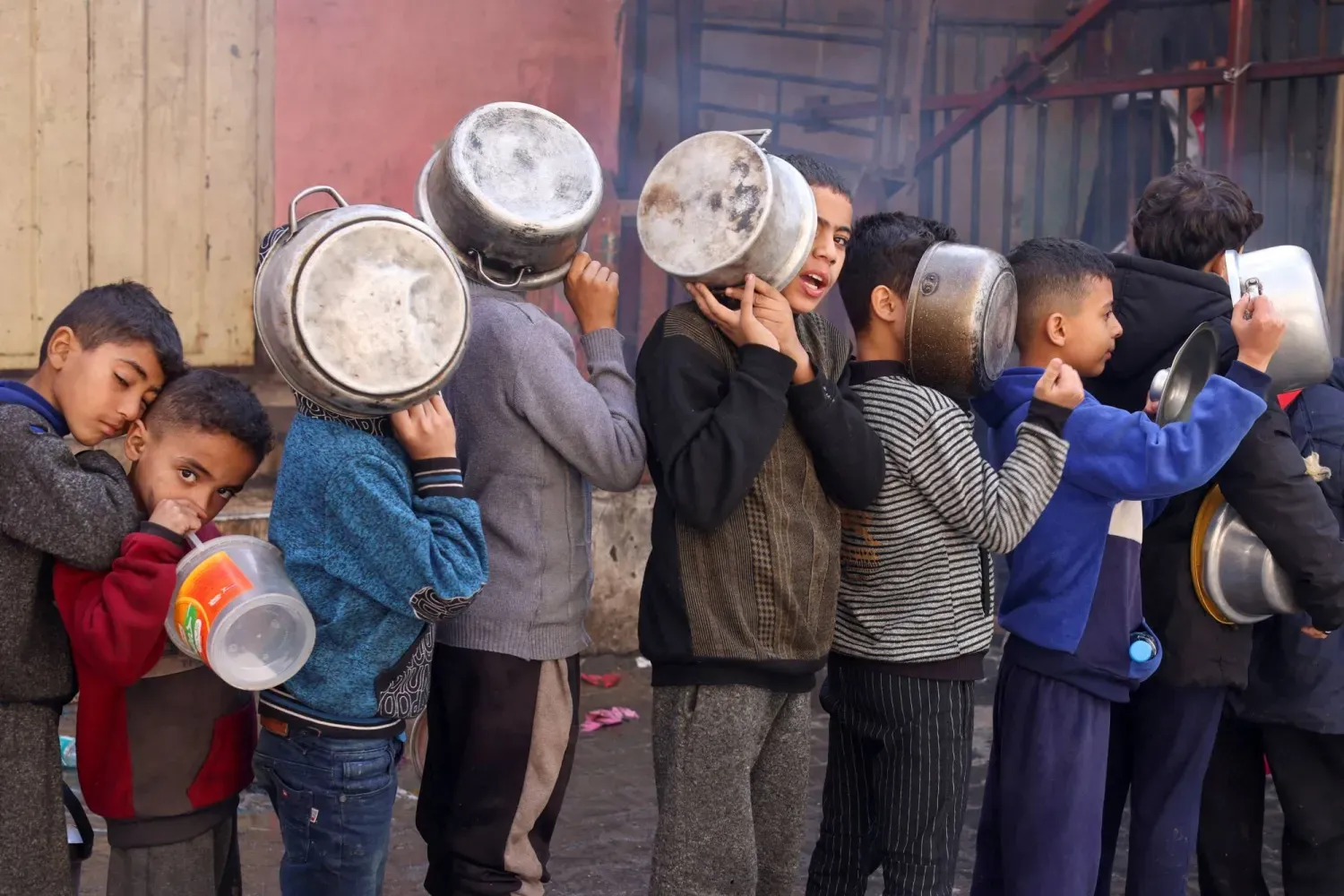 Gazze Şeridi'nin güneyindeki Refah'ta gıda sıkıntısı nedeniyle ellerinde tencerelerle pişmiş yiyecek bekleyen Filistinli çocuklar, (Reuters)