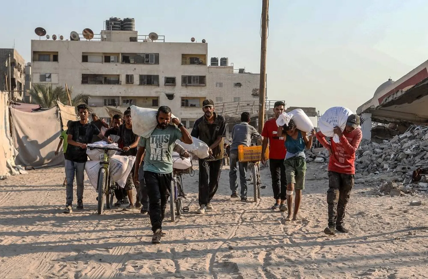 24 July 2025, Palestinian Territories, Khan Younis: Palestinians carrying bags of flour walk along a street in Khan Younis after trucks carrying humanitarian aid entered the southern Gaza Strip through the Israeli-controlled Kerem Shalom border crossing. (dpa)