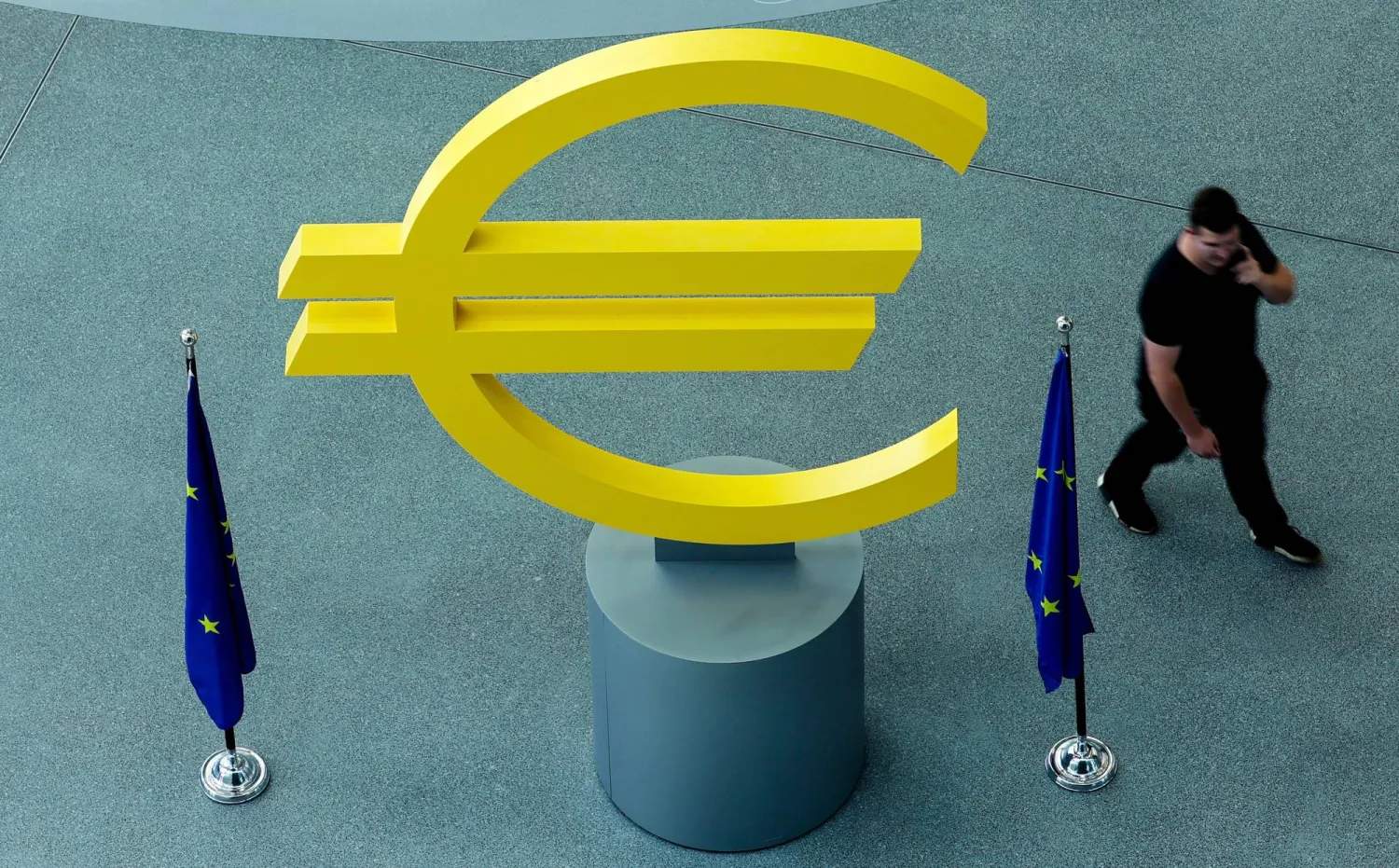 مجسم لعلامة العملة الأوروبية الموحدة وأعلام منطقة اليورو أمام مقر البنك المركزي الأوروبي في مدينة فرانكفورت الألمانية (إ.ب.أ)