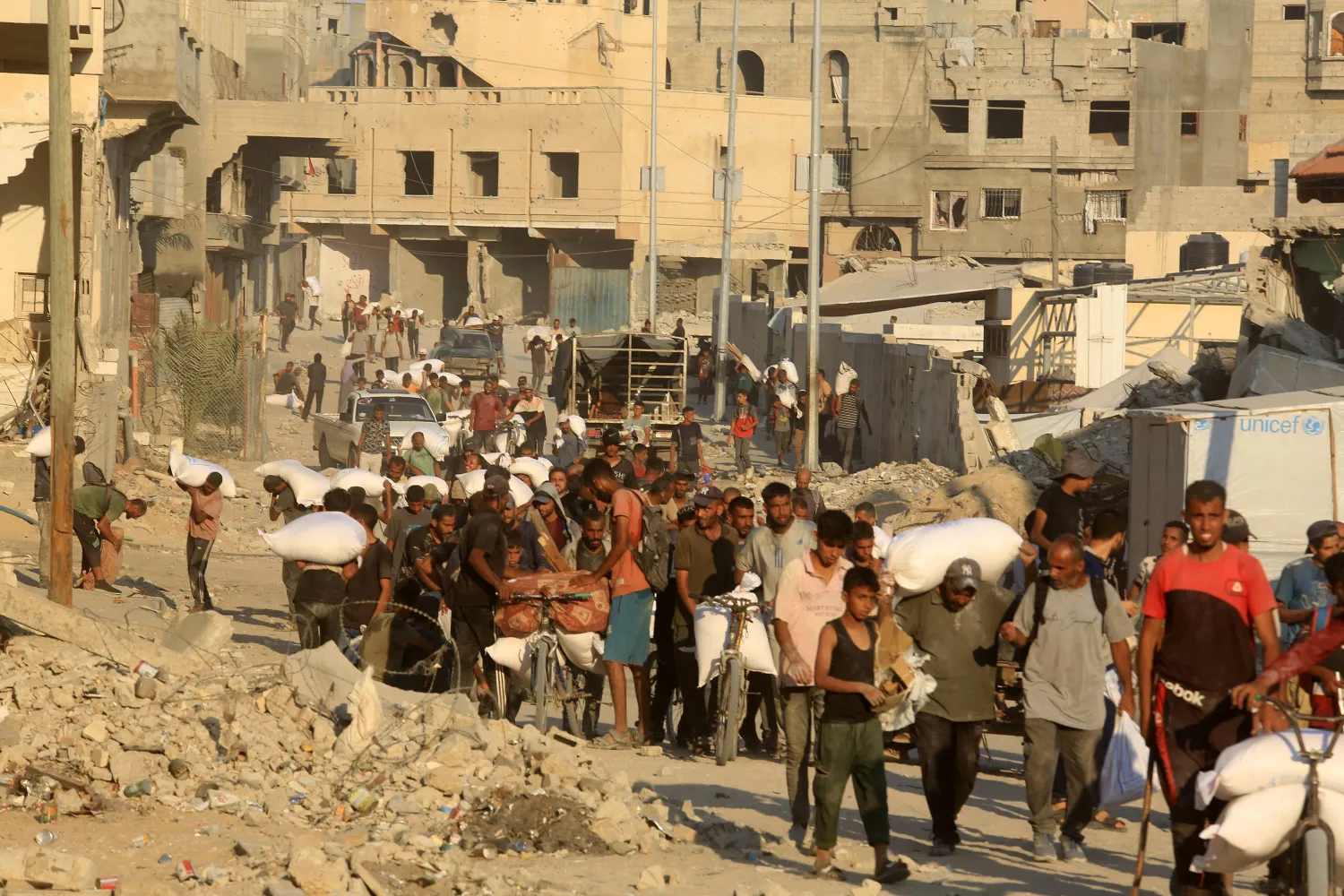 فلسطينيون يحملون أكياس الدقيق يسيرون في أحد شوارع خان يونس بغزة (د.ب.أ)