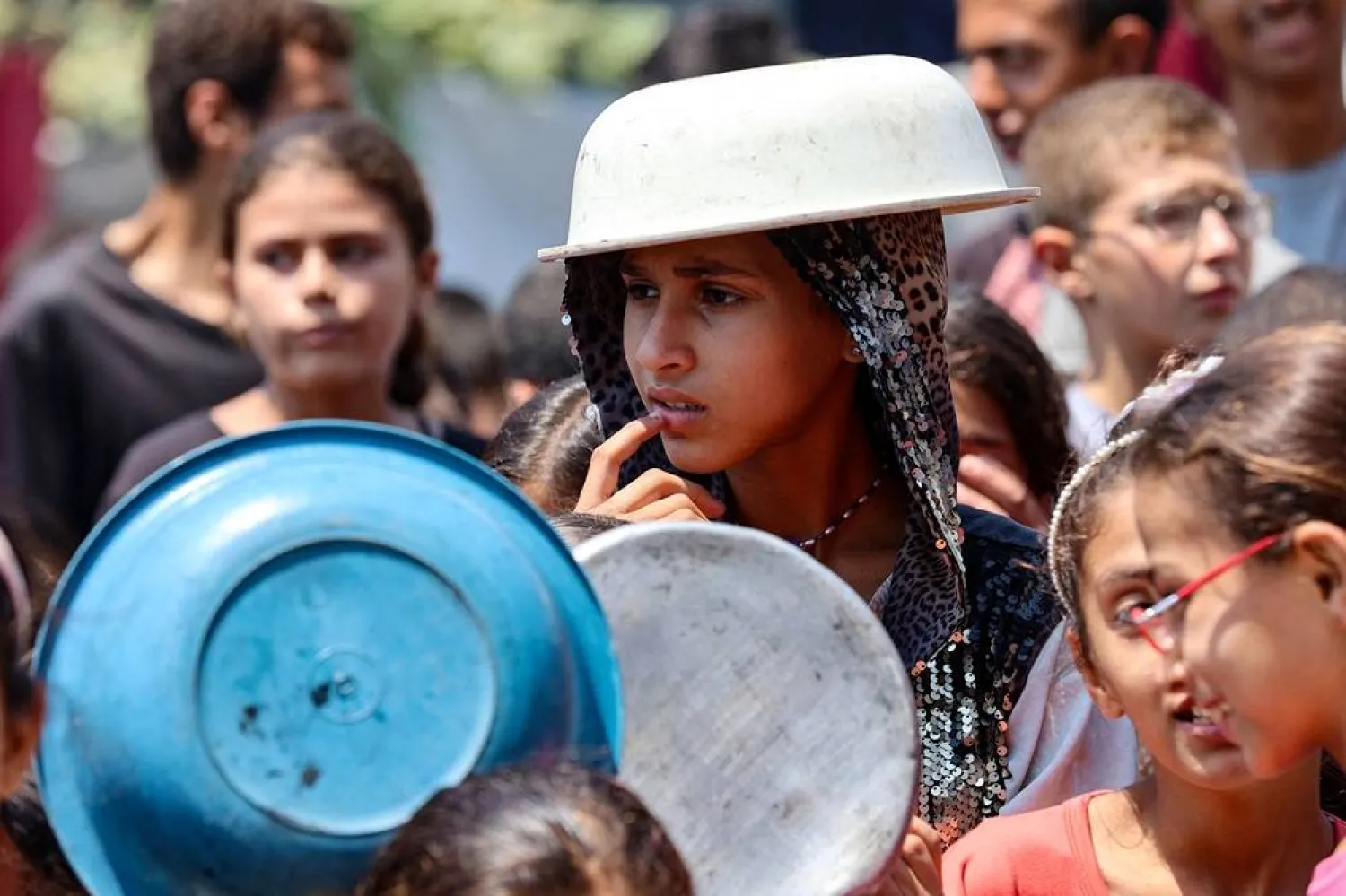 A displaced Palestinian girl covers her head with a pot to protect herself from the scorching sun as she waits at a food distribution point in Gaza City in the northern Gaza Strip on July 25, 2025. (AFP)