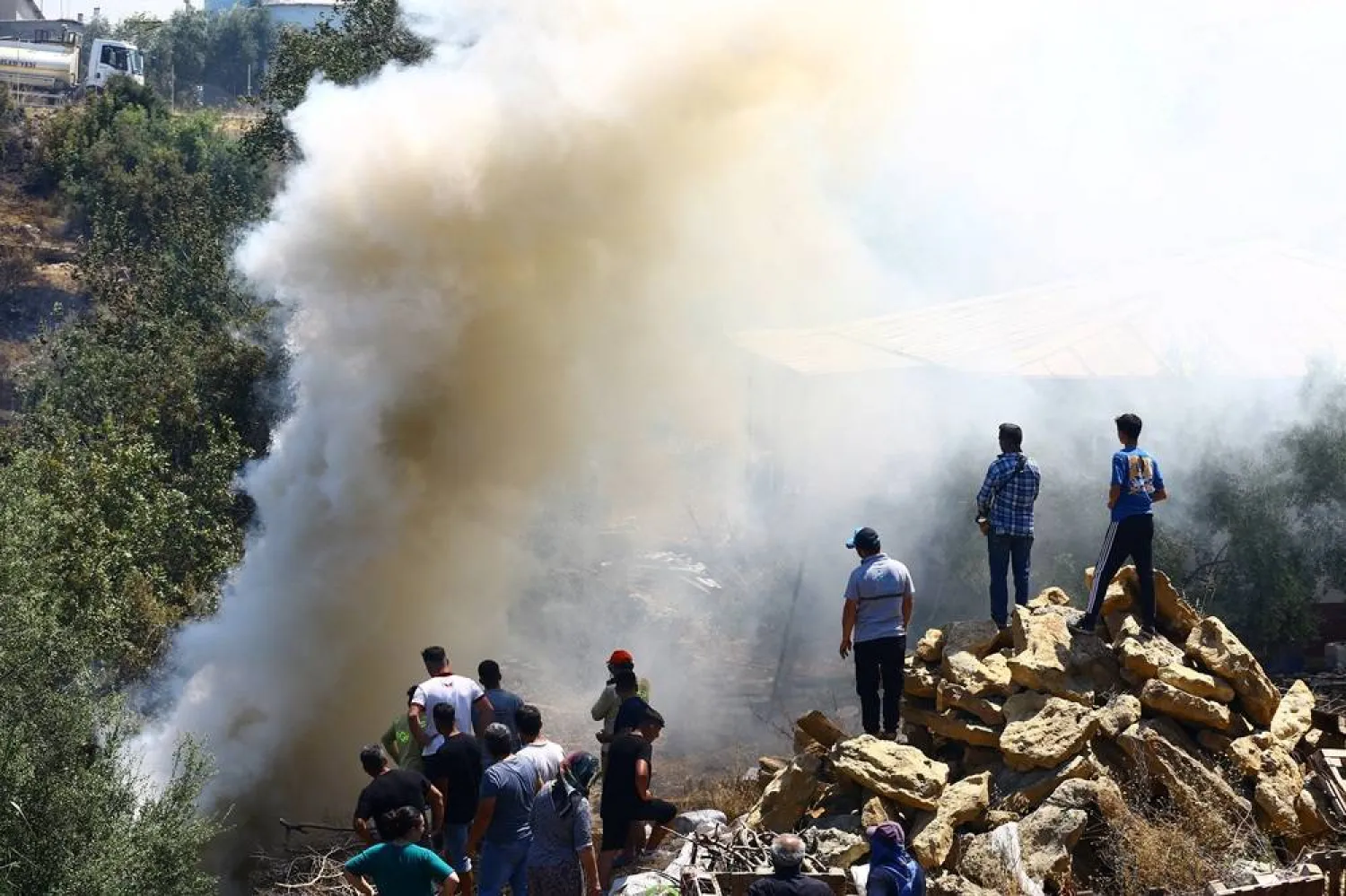 People stand next to smoke rising from the wildfire in the Aksu district of Antalya, a Mediterranean city in southern Türkiye, July 25, 2025. (Reuters) 