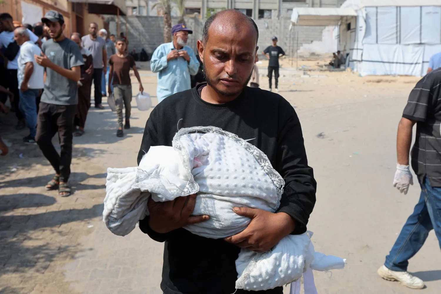 فلسطيني يحمل جثة طفله الذي توفى جراء الجوع في خان يونس السبت (رويترز)