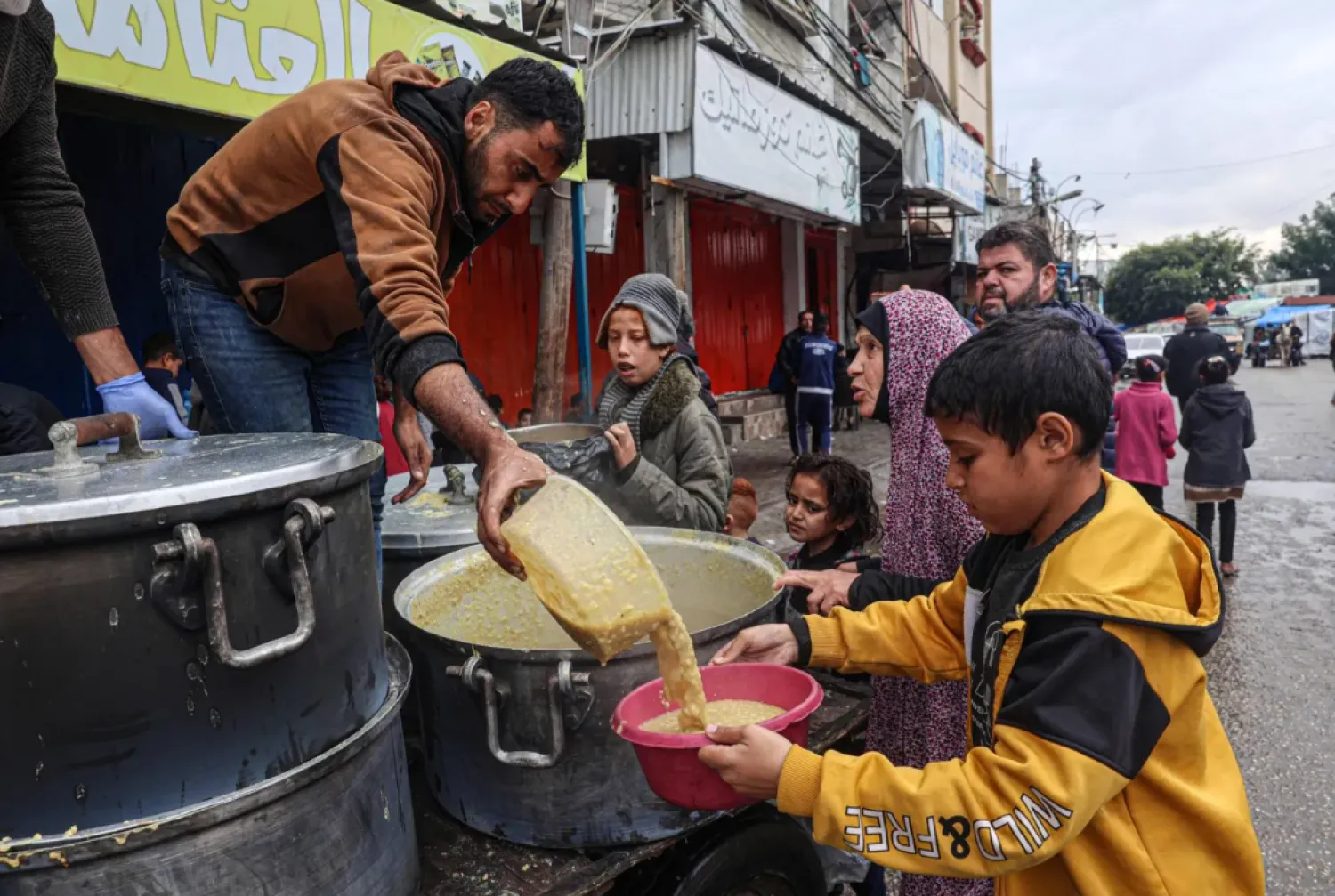 A volunteer distributes rations of red lentil soup to displaced Palestinians in Rafah in the southern Gaza Strip on February 18, 2024. (Photo by SAID KHATIB / AFP)
