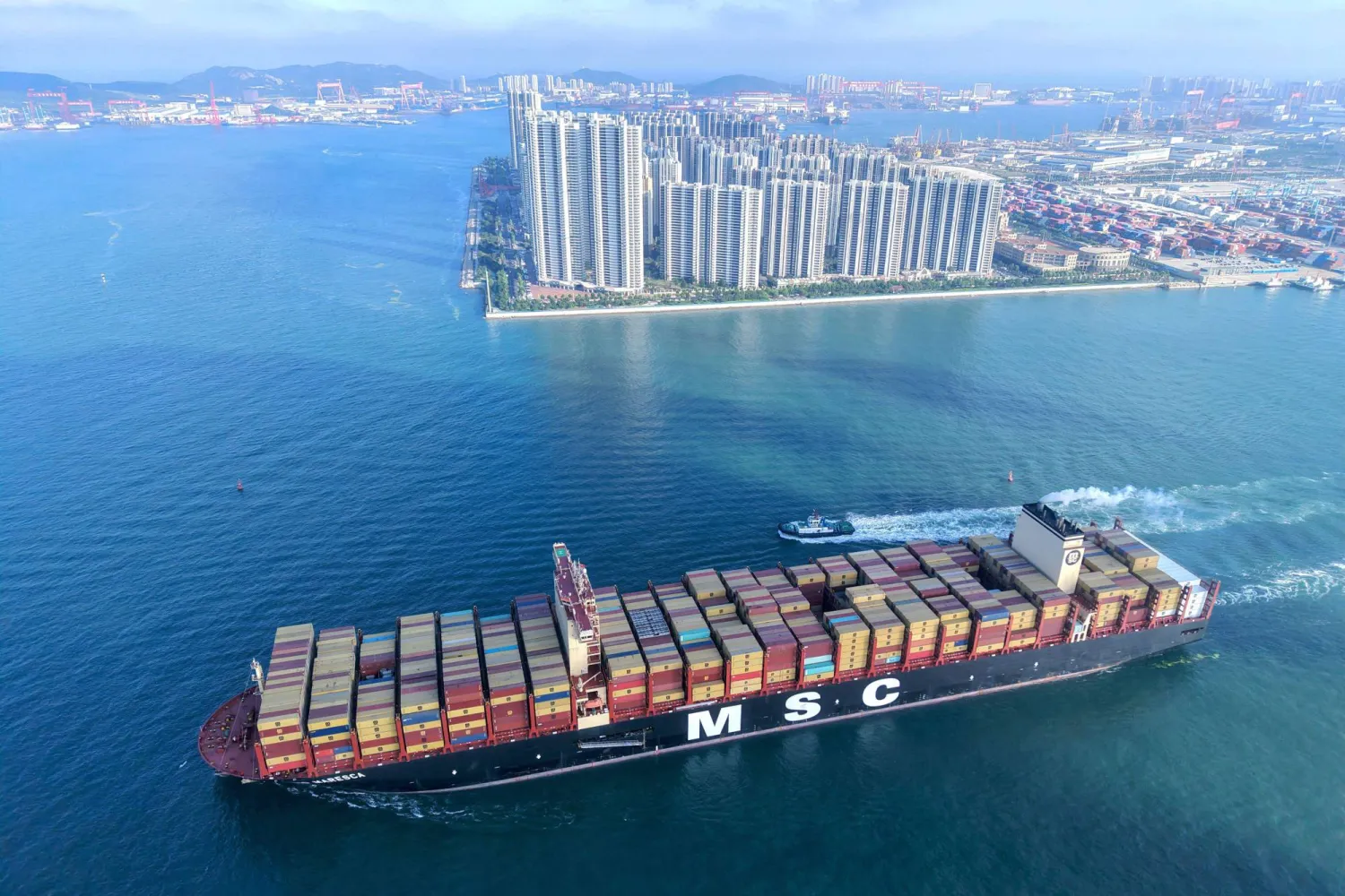 سفينة حاويات تبحر بالقرب من مبانٍ في تشينغداو في مقاطعة شاندونغ شرق الصين (أ.ف.ب)