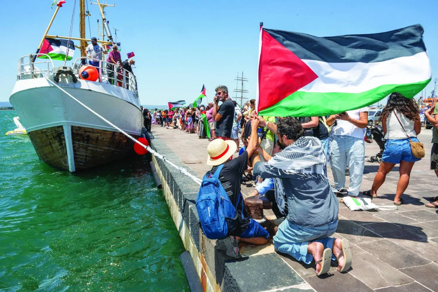 People gather with Palestinian flags around the Freedom Flotilla ship "Handala" ahead of the boat's departure for Gaza at a port in Syracuse, Sicily, southern Italy, on July 13, 2025. (Photo by Giovanni ISOLINO / AFP)