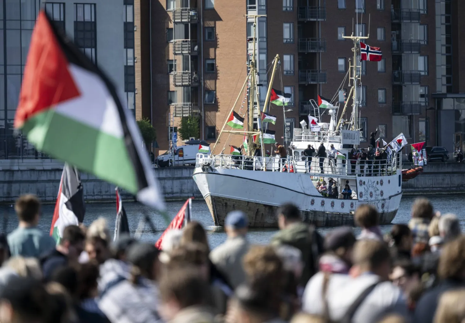 متظاهرون يحملون أعلاماً فلسطينية ينظرون إلى السفينة «حنظلة» المتجهة إلى غزة وهي تصل إلى ميناء مالمو بالسويد (أ.ب)