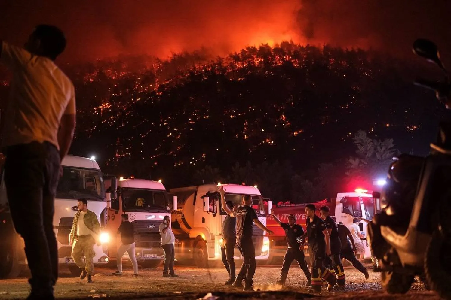 Residents and firefighters attempt to extinguish a wildfire as smoke and flames rise from a forested area in the Gursu district of Bursa early on July 27, 2025. (AFP) 