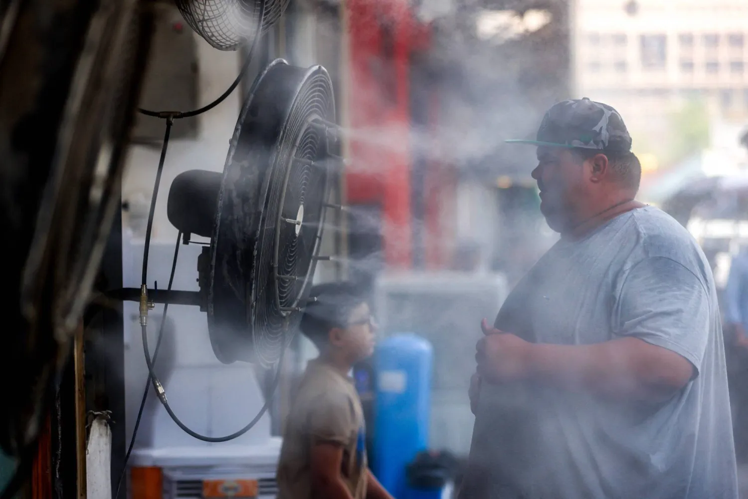 عراقي يقف أمام مروحة تضخ مياهاً لتبريد جسمه في منطقة السنك بالعاصمة العراقية بغداد (أ.ف.ب)